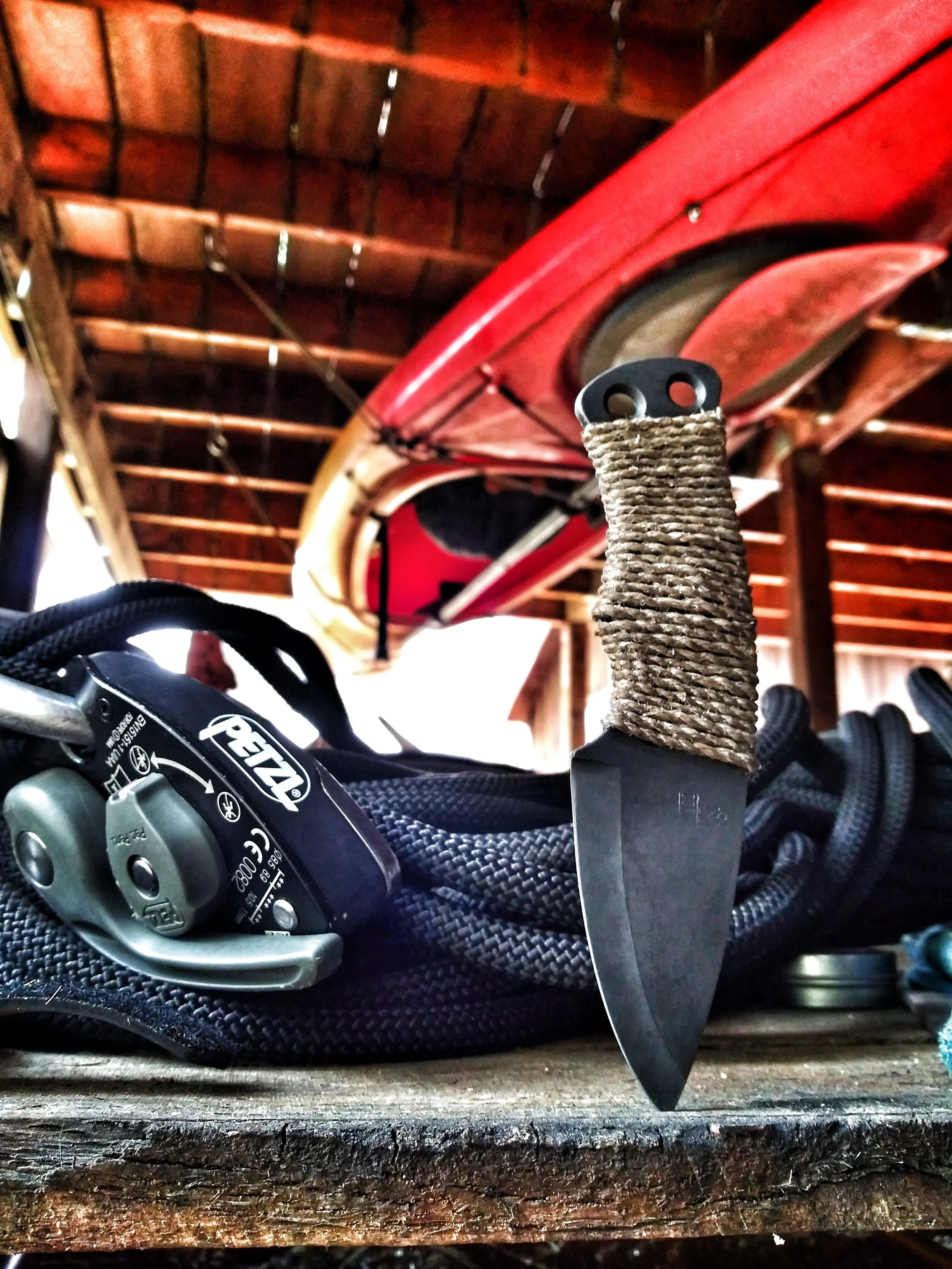 A knife lodged in wood in front of a rope.