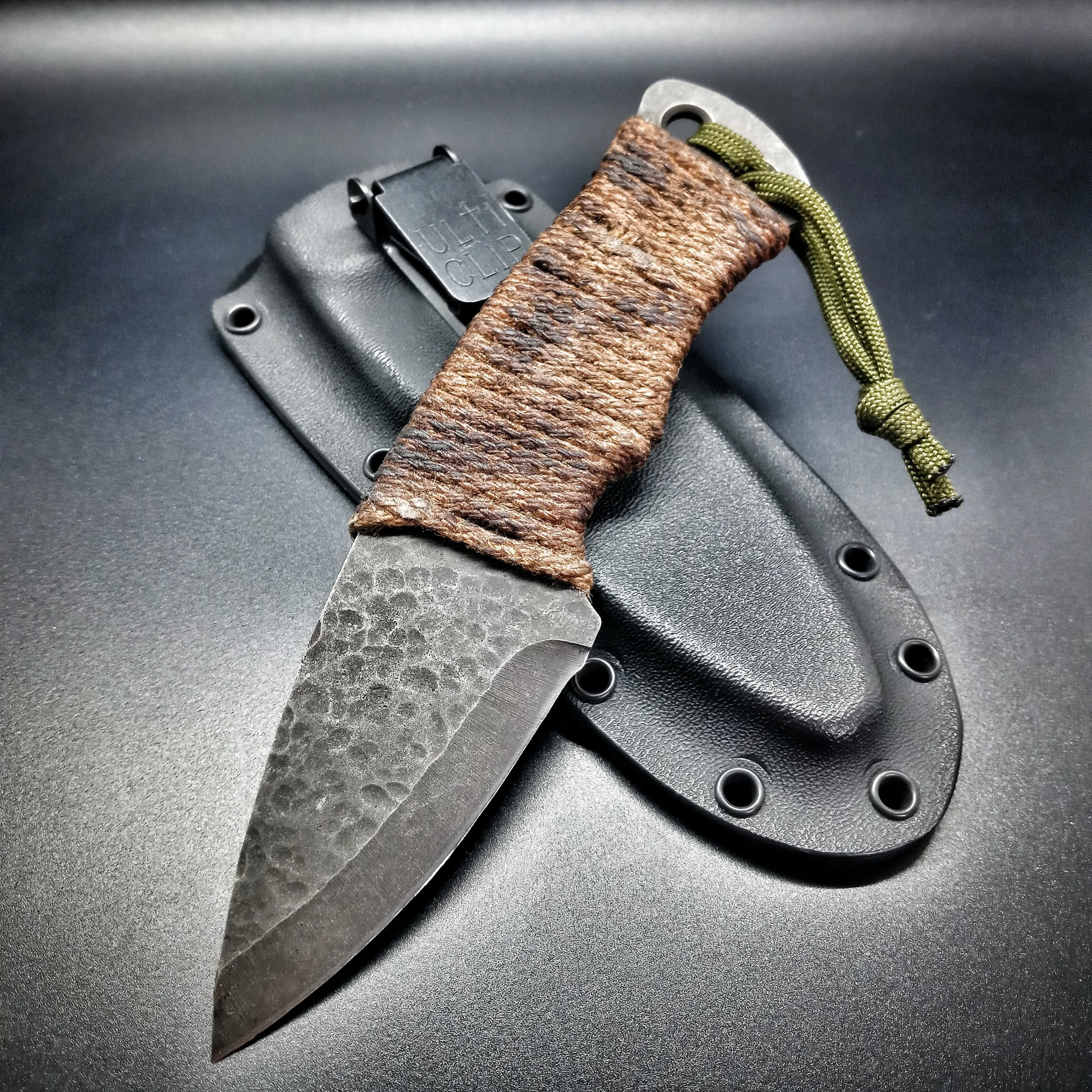 A knife with a hammered finish resting on its sheath.