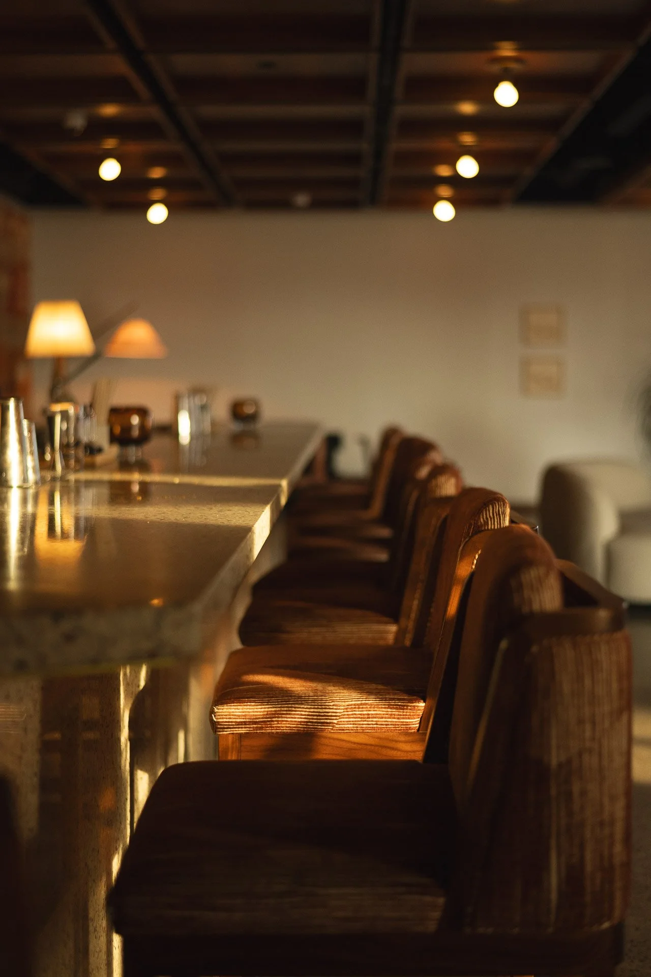 A row of wooden barstools with upholstered seats beside a marble-top bar counter in a dimly lit lounge or bar.