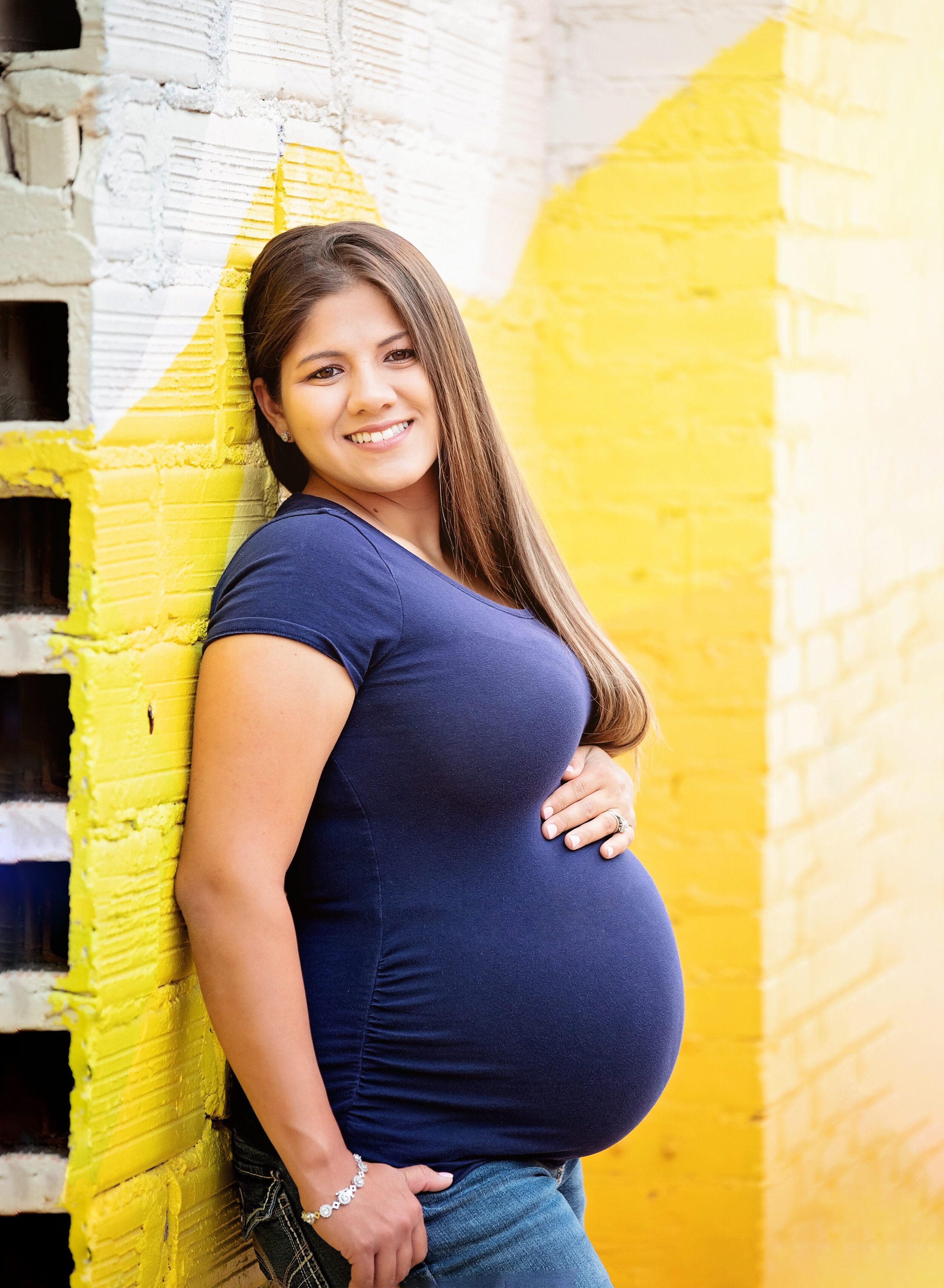 Pregnant mom leaning on yellow wall on Texas Avenue in Baytown. 