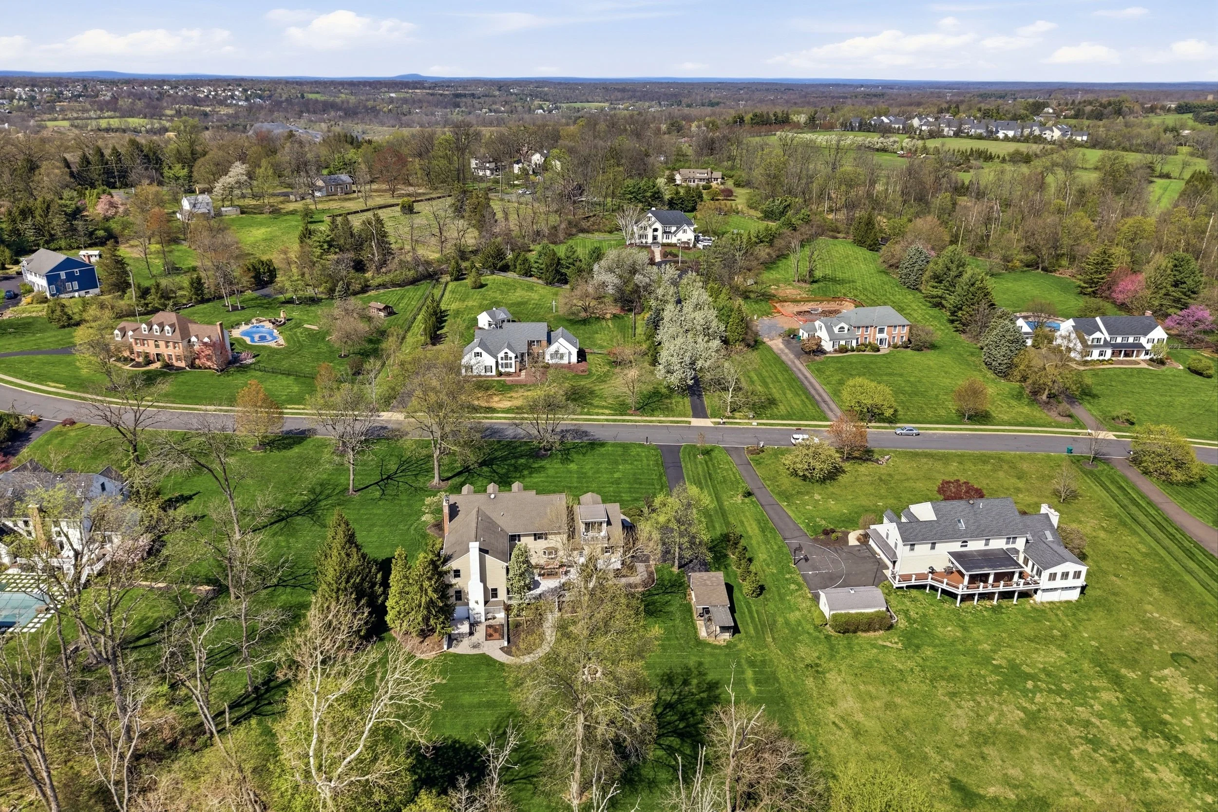 An aerial view of a suburban neighborhood with houses, green lawns, and trees under a partly cloudy sky.