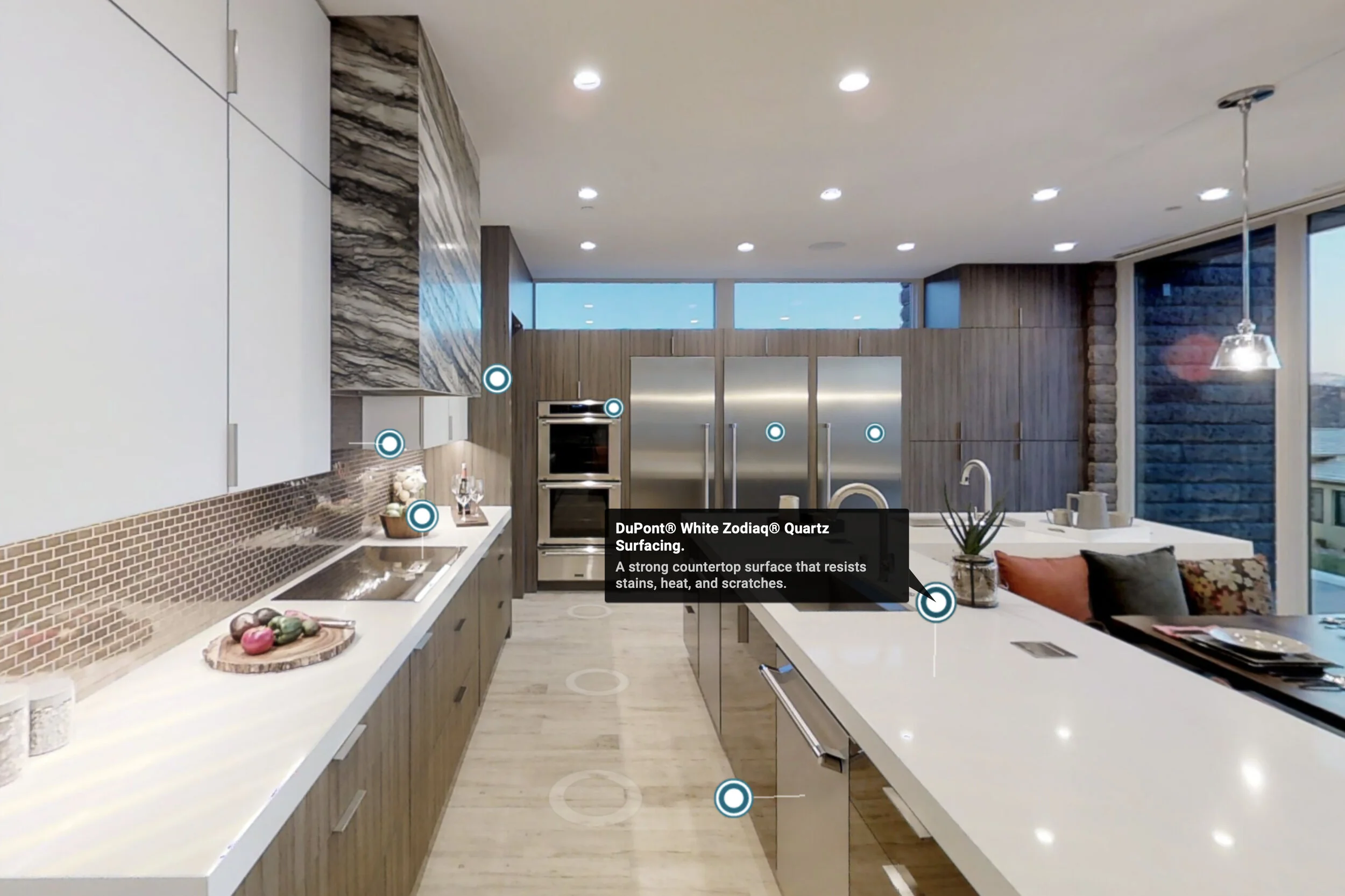 Modern kitchen with white countertops, wood cabinetry, stainless steel appliances, and a tile backsplash. There are recessed ceiling lights and large windows letting in natural light.