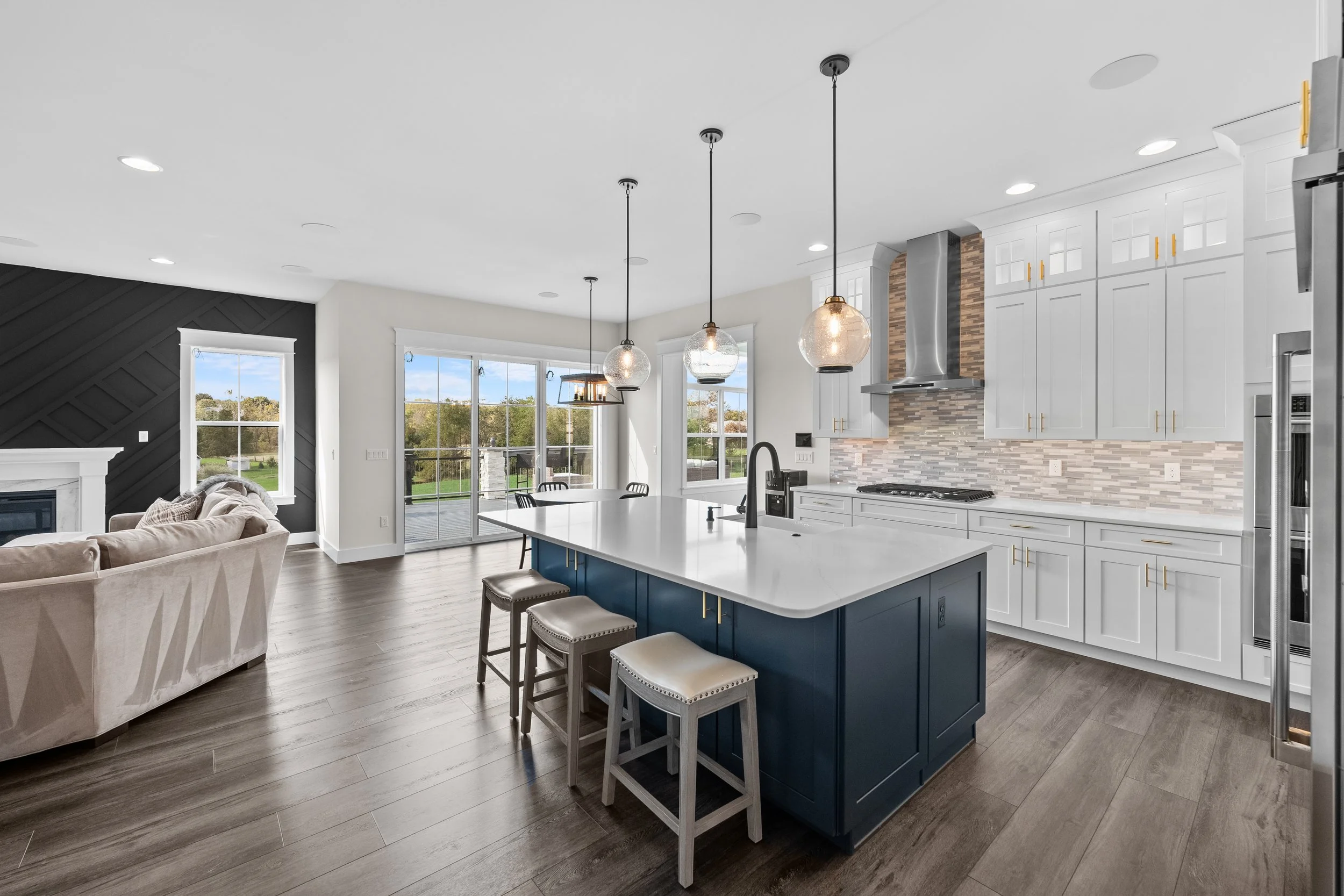 Modern kitchen with island, white cabinets, brick backsplash, pendant lights, and large windows with a view of outdoors.