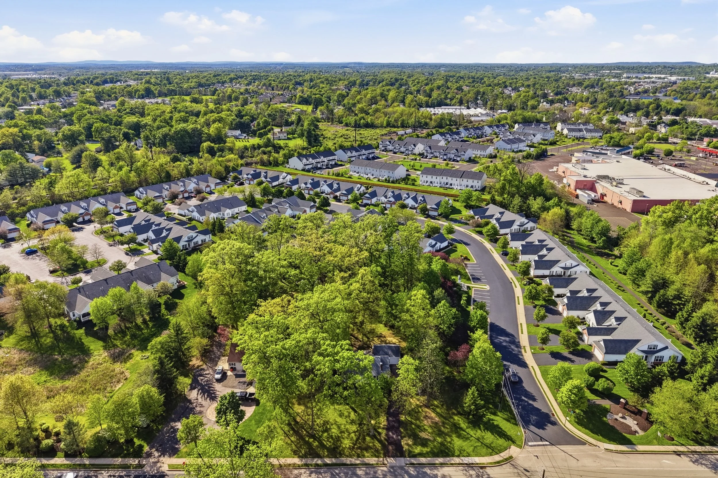 An aerial view of a suburban neighborhood with houses, trees, and streets, and a commercial building with a large parking lot.