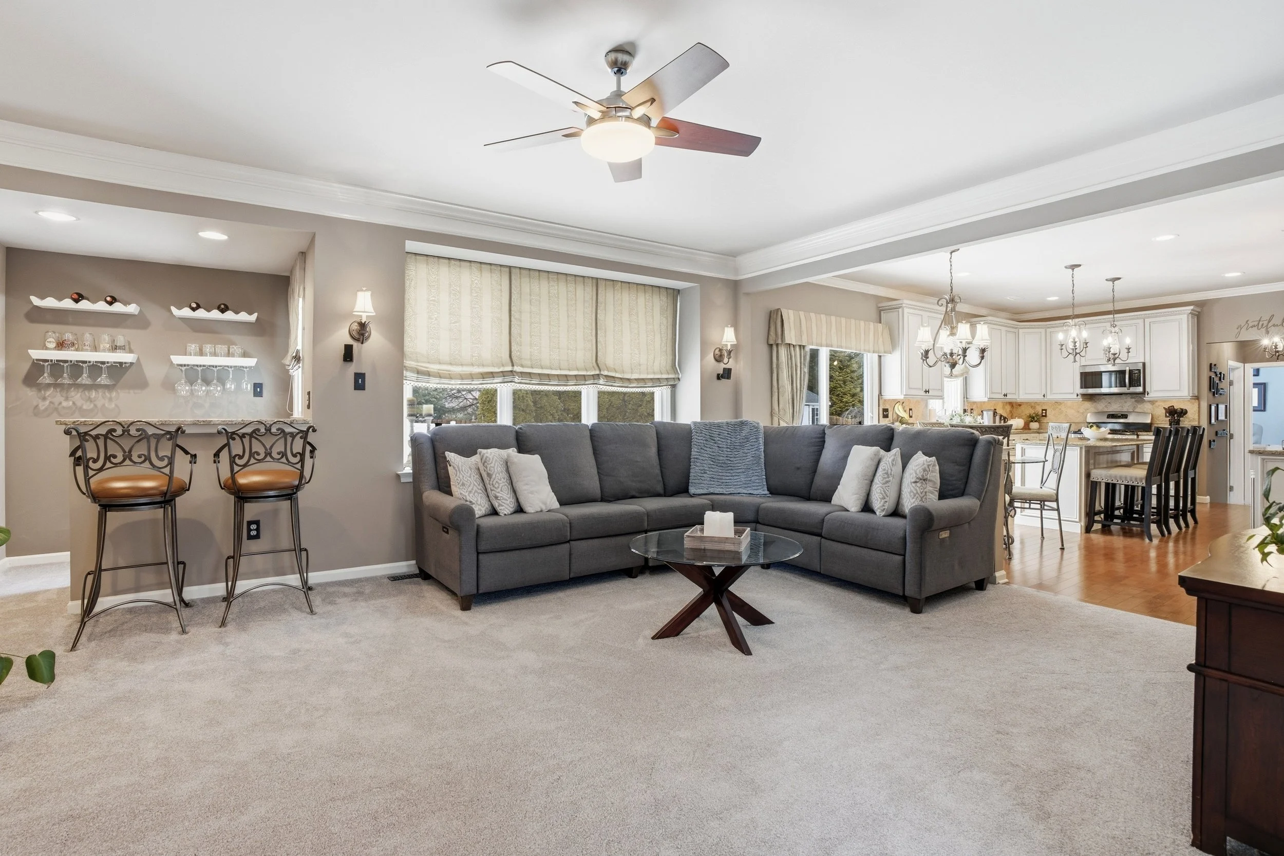 Open-concept living room and kitchen with a ceiling fan, gray sectional sofa, and kitchen cabinetry with a dining area.