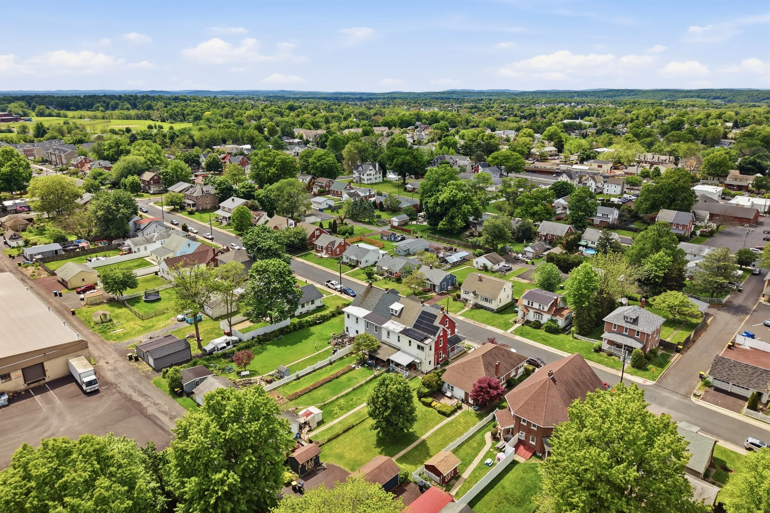 Aerial view of a suburban neighborhood with houses, trees, streets, and green spaces on a sunny day.