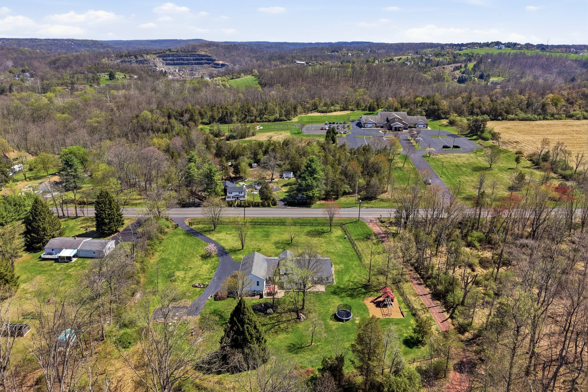 Aerial view of a suburban area with houses, trees, and a large parking lot, surrounded by rolling hills and forests.