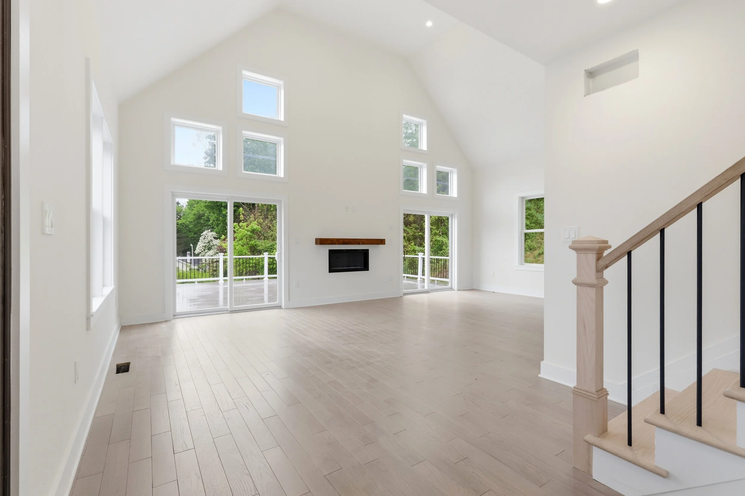 Bright, spacious living area with large windows, hardwood floors, a fireplace, and a staircase.