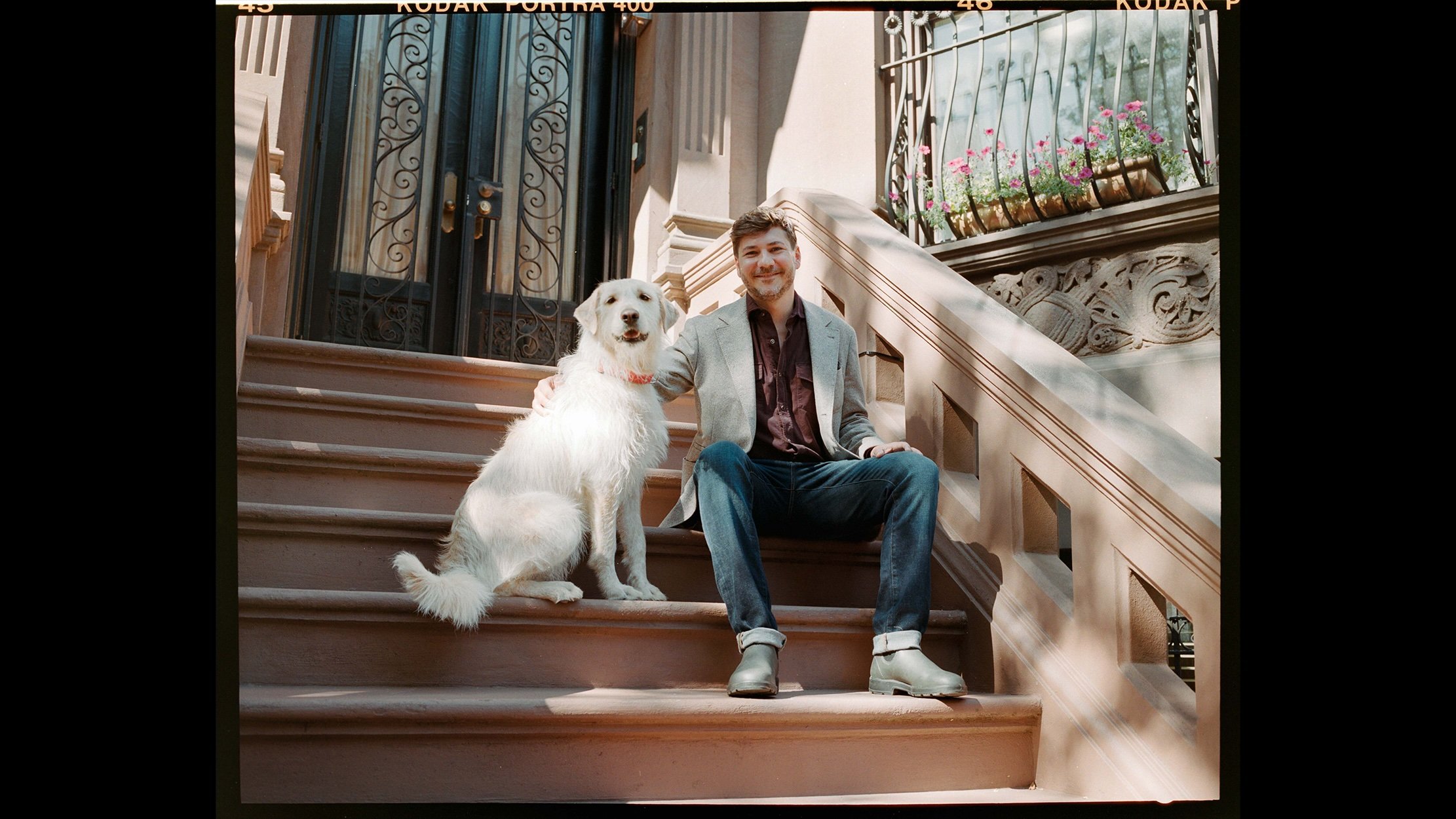 PJ Smith is sitting outside of stair with his fluffy white dog.