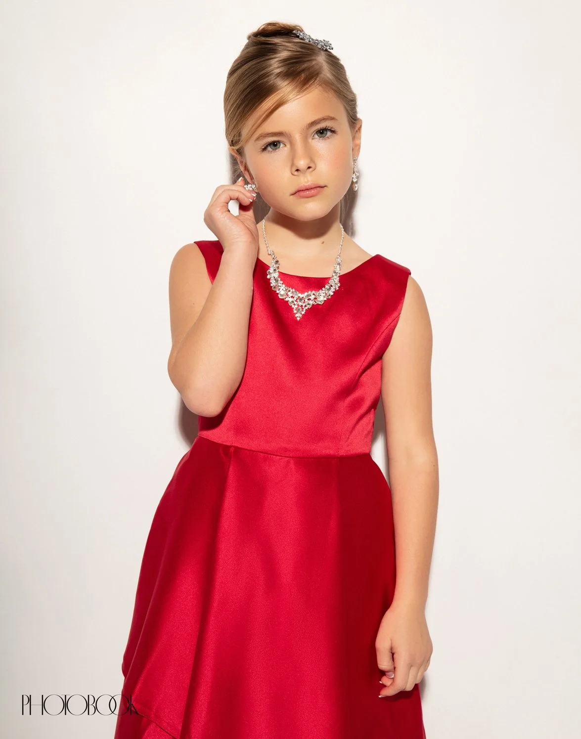 A image of a young child wearing a sheer red dress and crystal jewelry.