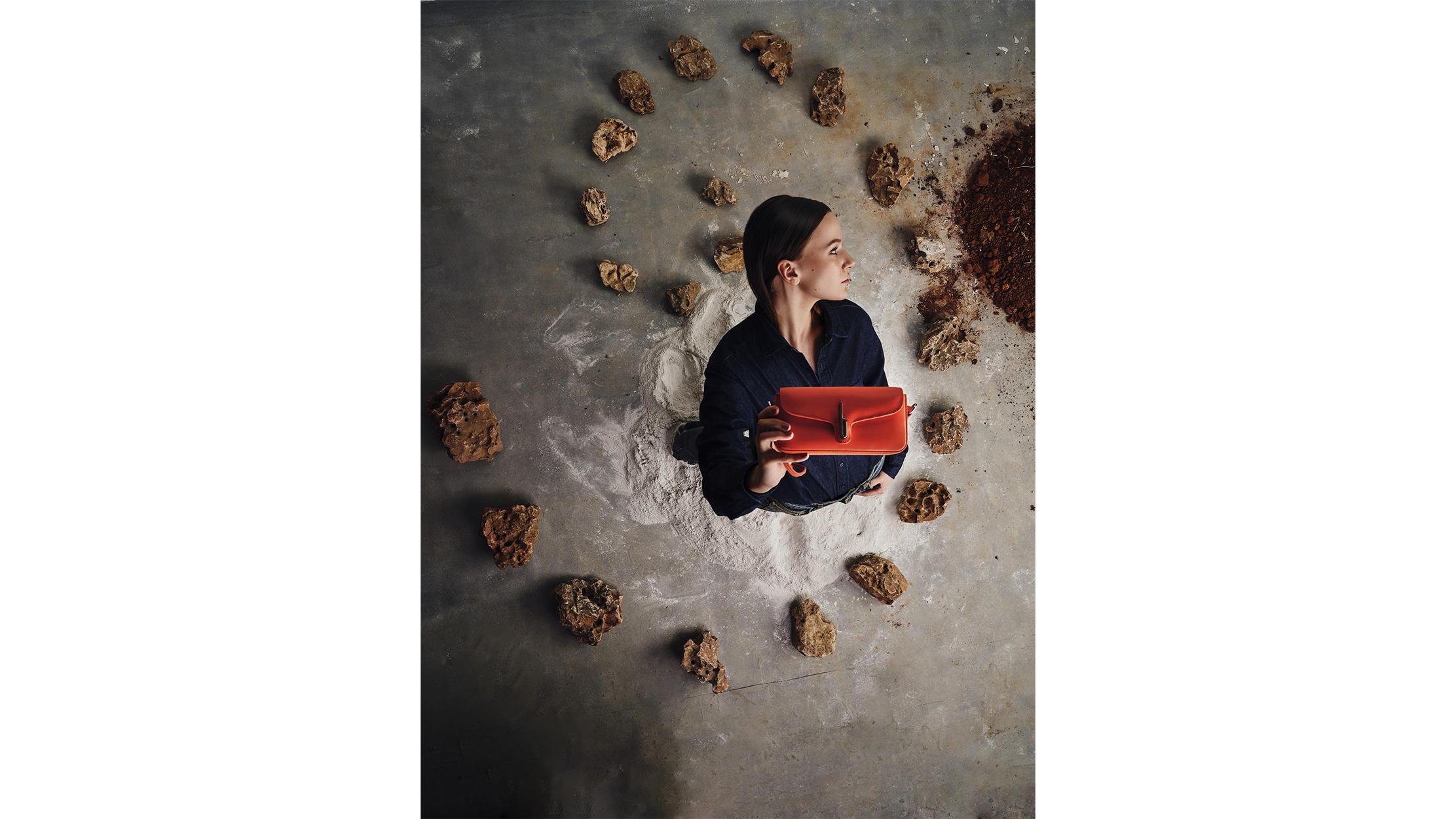 Woman holding red bag, surrounded in a circle of rocks.
