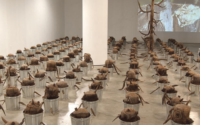 The Last Tree is a monumental installation of 193 tree stump sculptures encased in metal pails and placed in a grid formation to transform the gallery space into a barren landscape. The number of stumps corresponds to that of the countries in the world, namely, those members of the United Nations. One large tree rises from the grid, as a symbol of the “last tree,” which is in danger of its extinction from the earth. The devastated stumps are poised to witness the destruction of the “last tree” – a fate that humanity is bringing onto itself. Accompanying video projections and sounds amplify the urgency of the situation. The Last Tree was shown at the ISE Cultural Center in 2013 and traveled to the Birchfield Penney Art Center in 2016. ISE Cultural Center