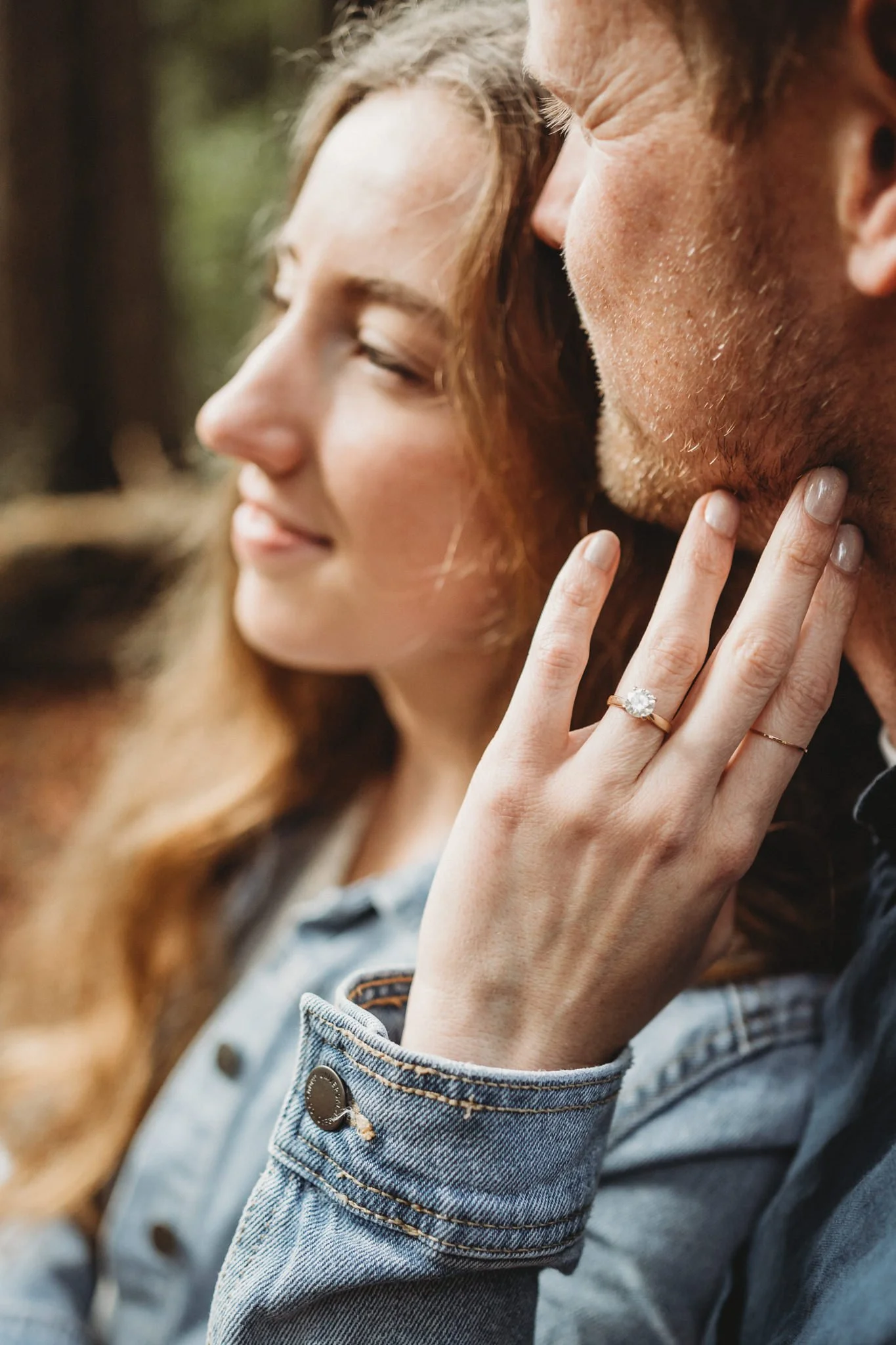 Close-up of a couple demonstrating a wedding ring on the woman's finger, with the woman's hand gently touching the man's face, both appearing to enjoy a tender moment.