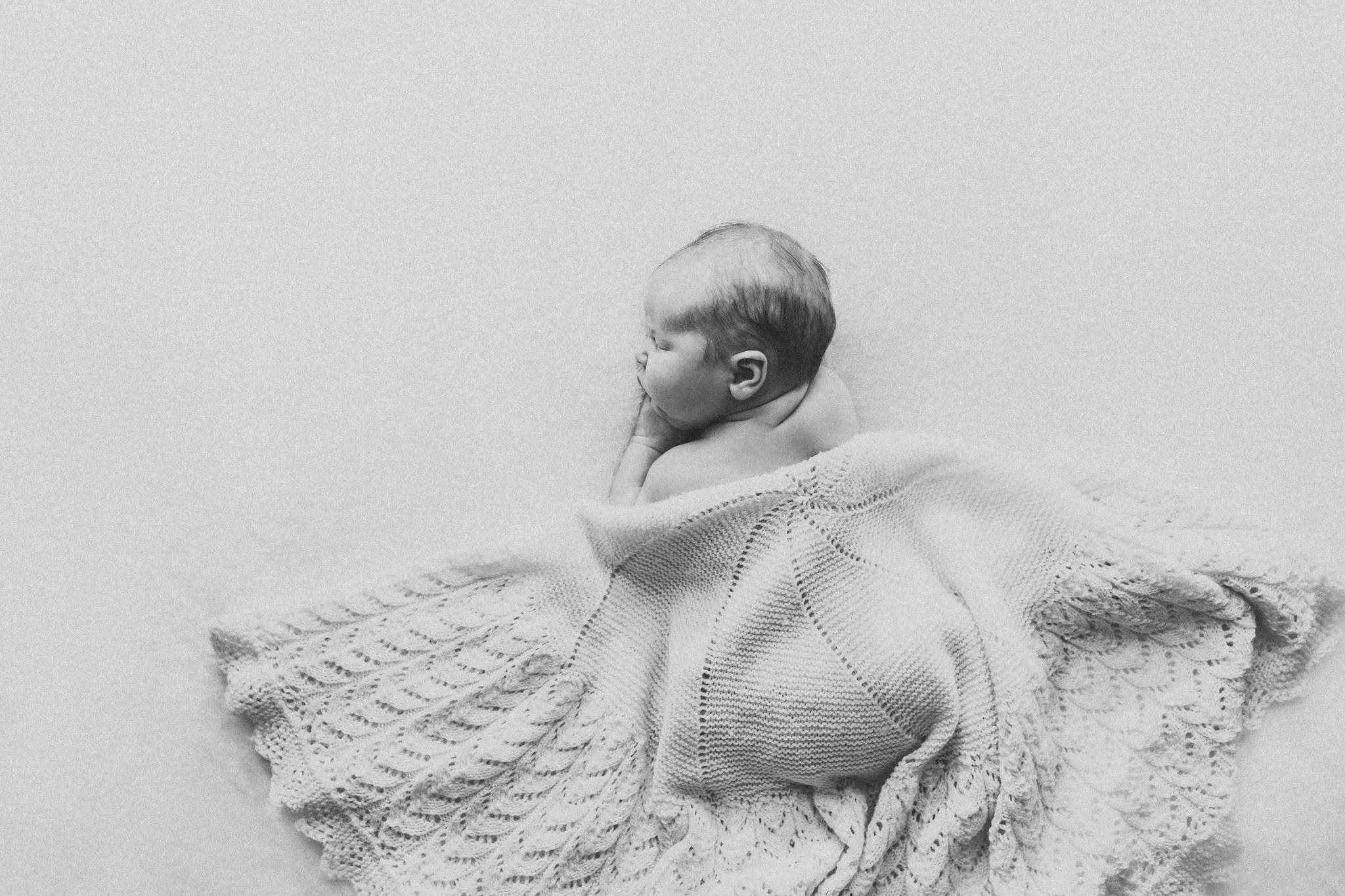 Black and white photo of baby on a beanbag. Styled prop blanket on top of baby.