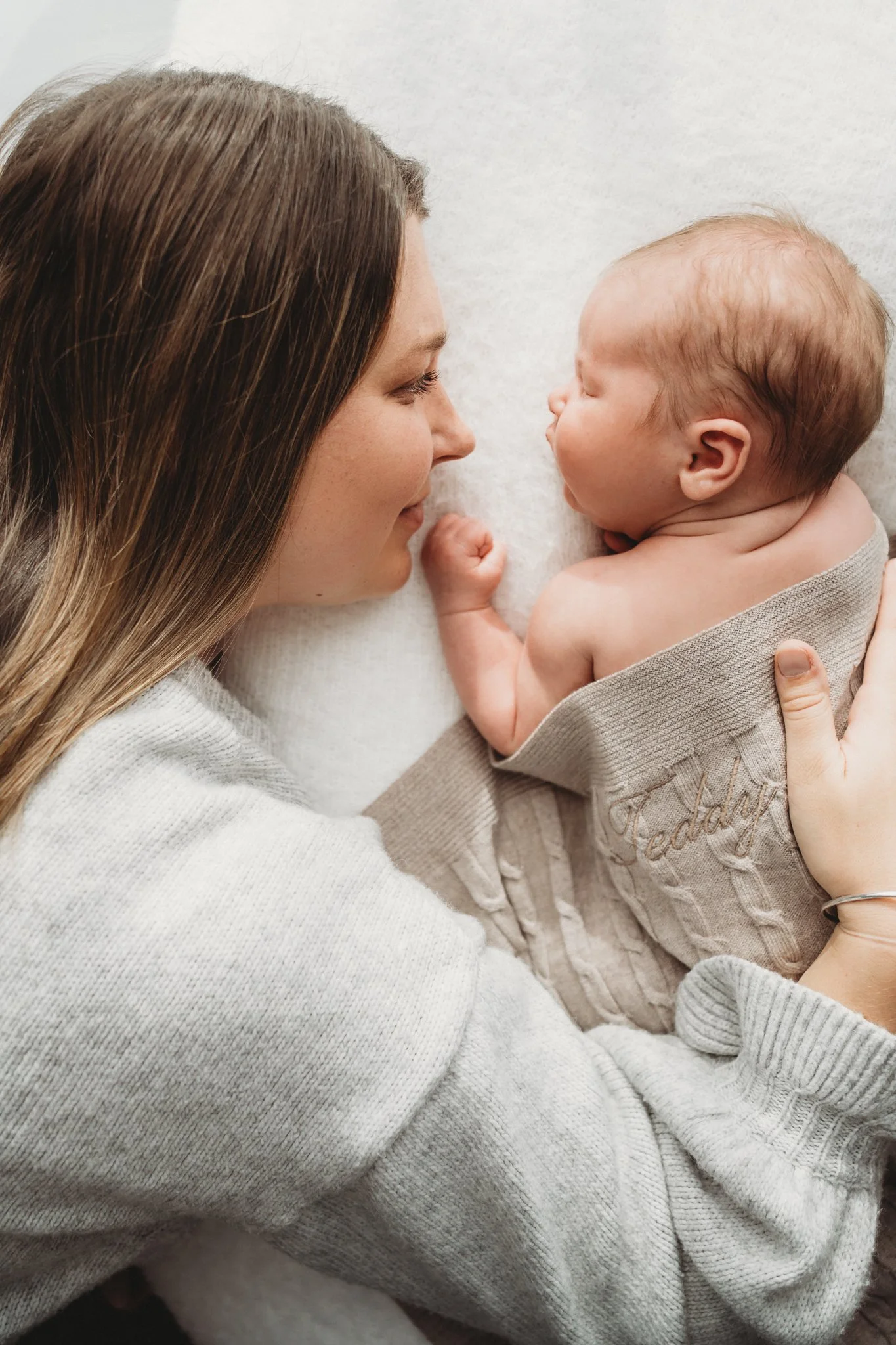Side profiles of mum and her newborn baby snuggling together on a timeless neutral backrop