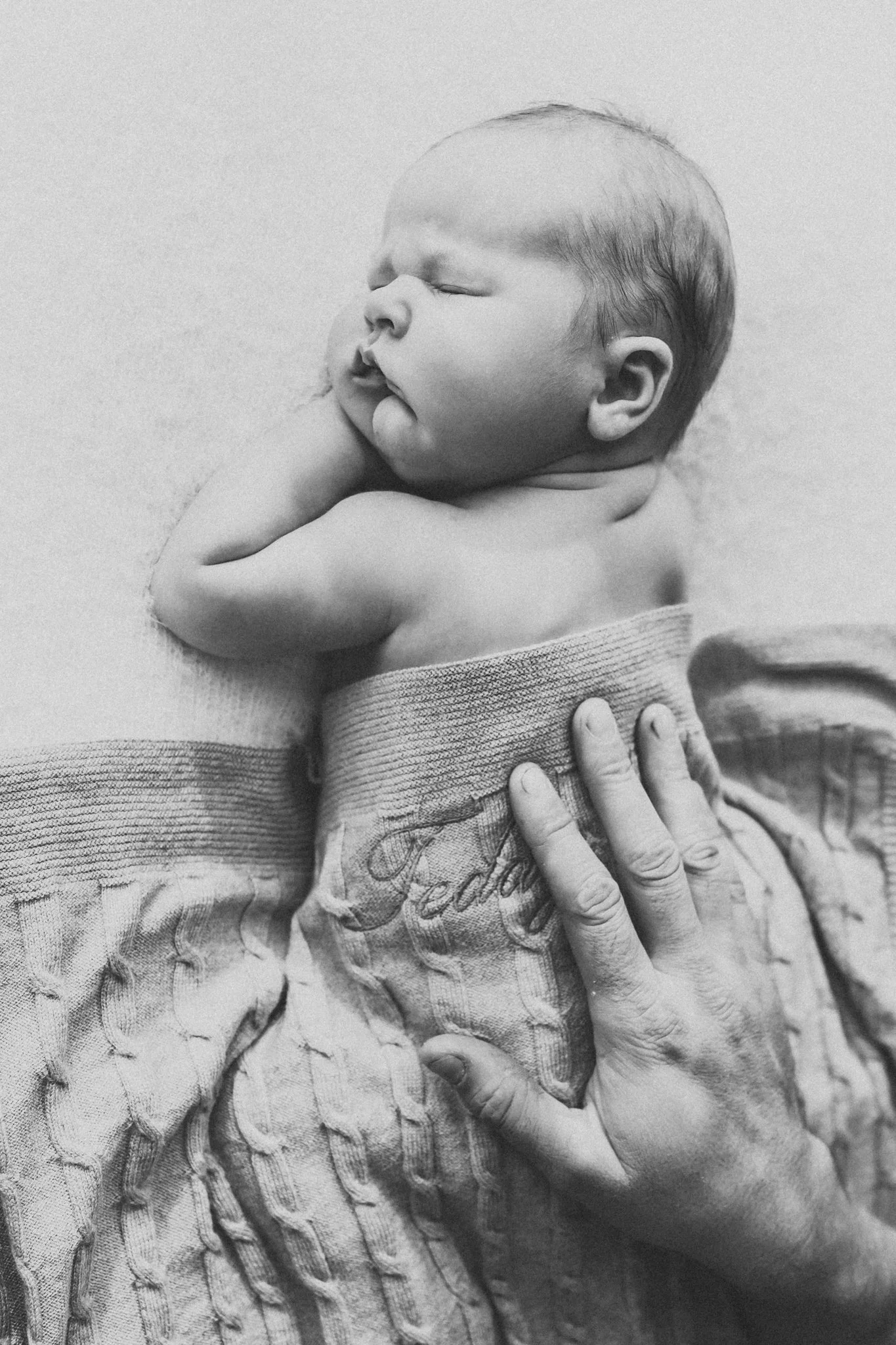 Black and white close up image of dad's hand on baby's back