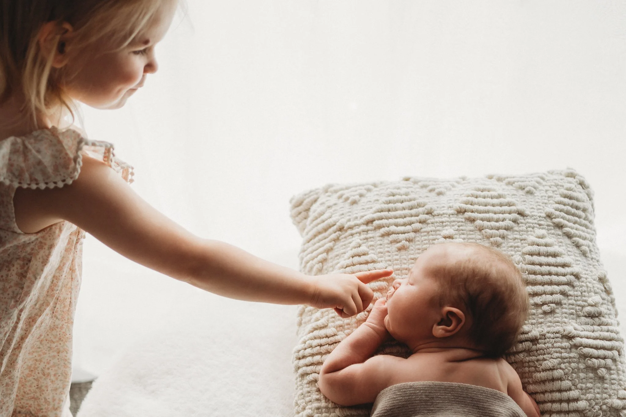 Sibling touches her new sister on the nose. Timeless white backdrop