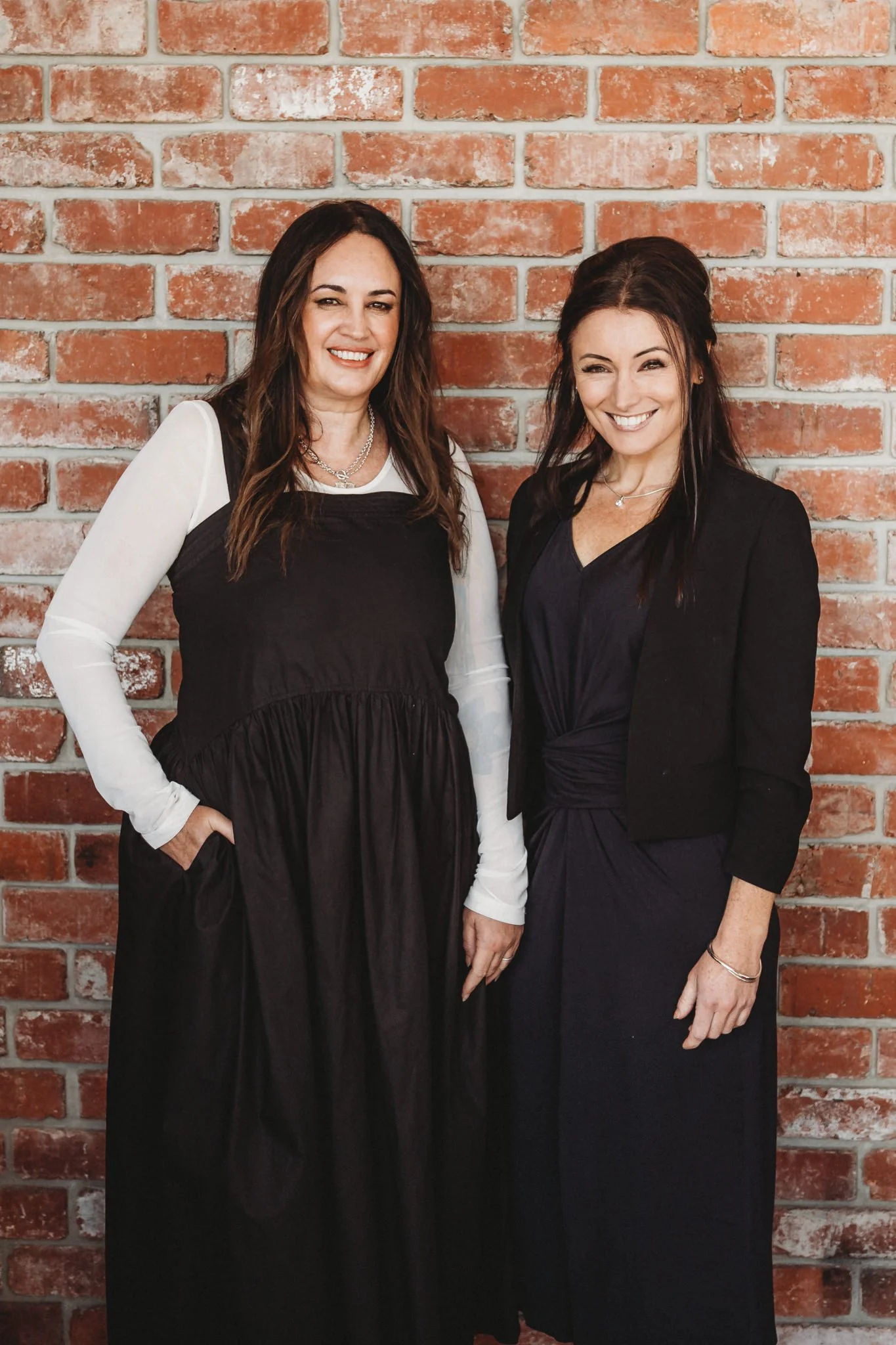 Two business owners side by side against a brick wall.