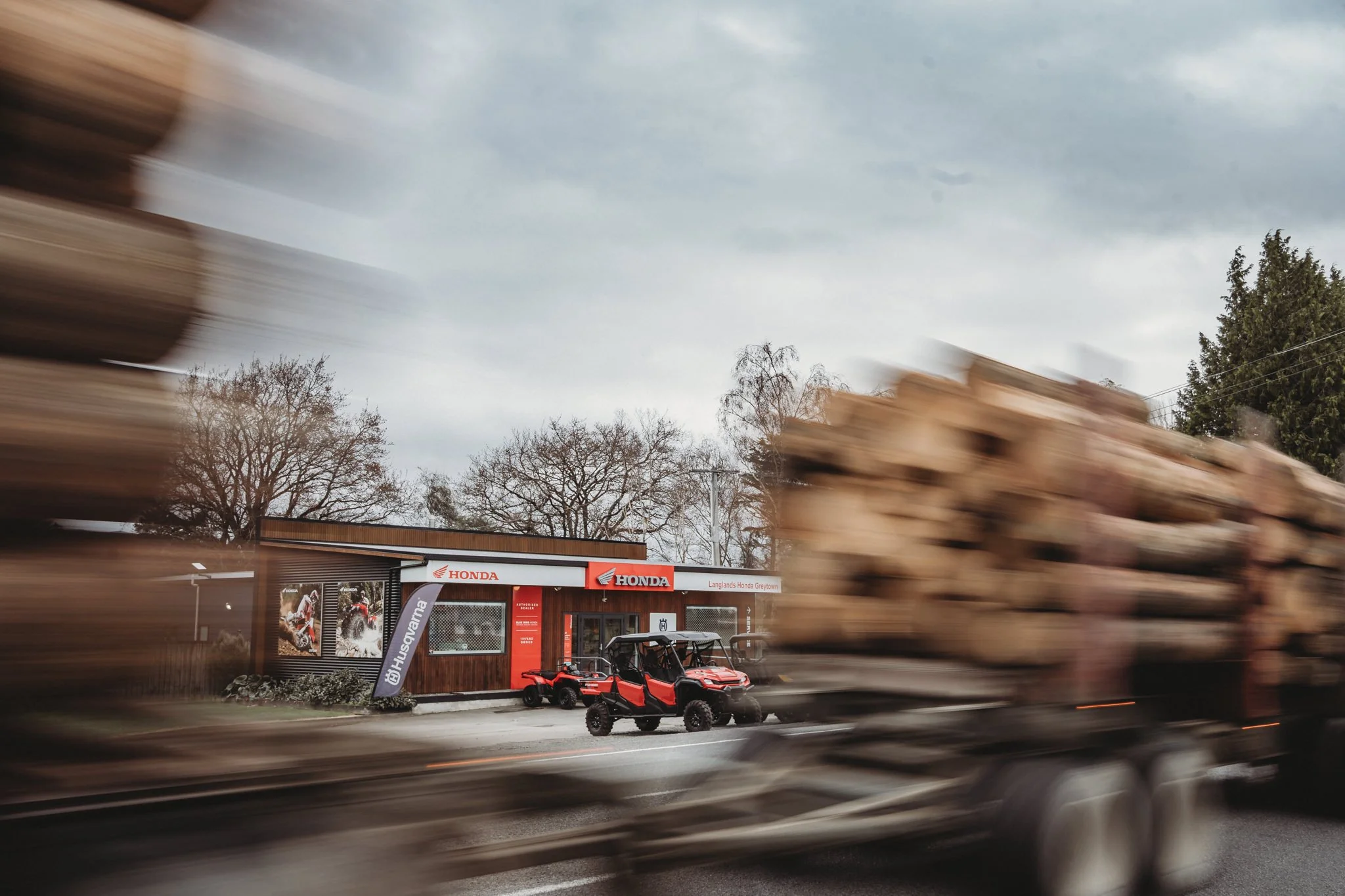Exterior shot of Langlands Greytown branch. Motion blurred logging truck in foreground
