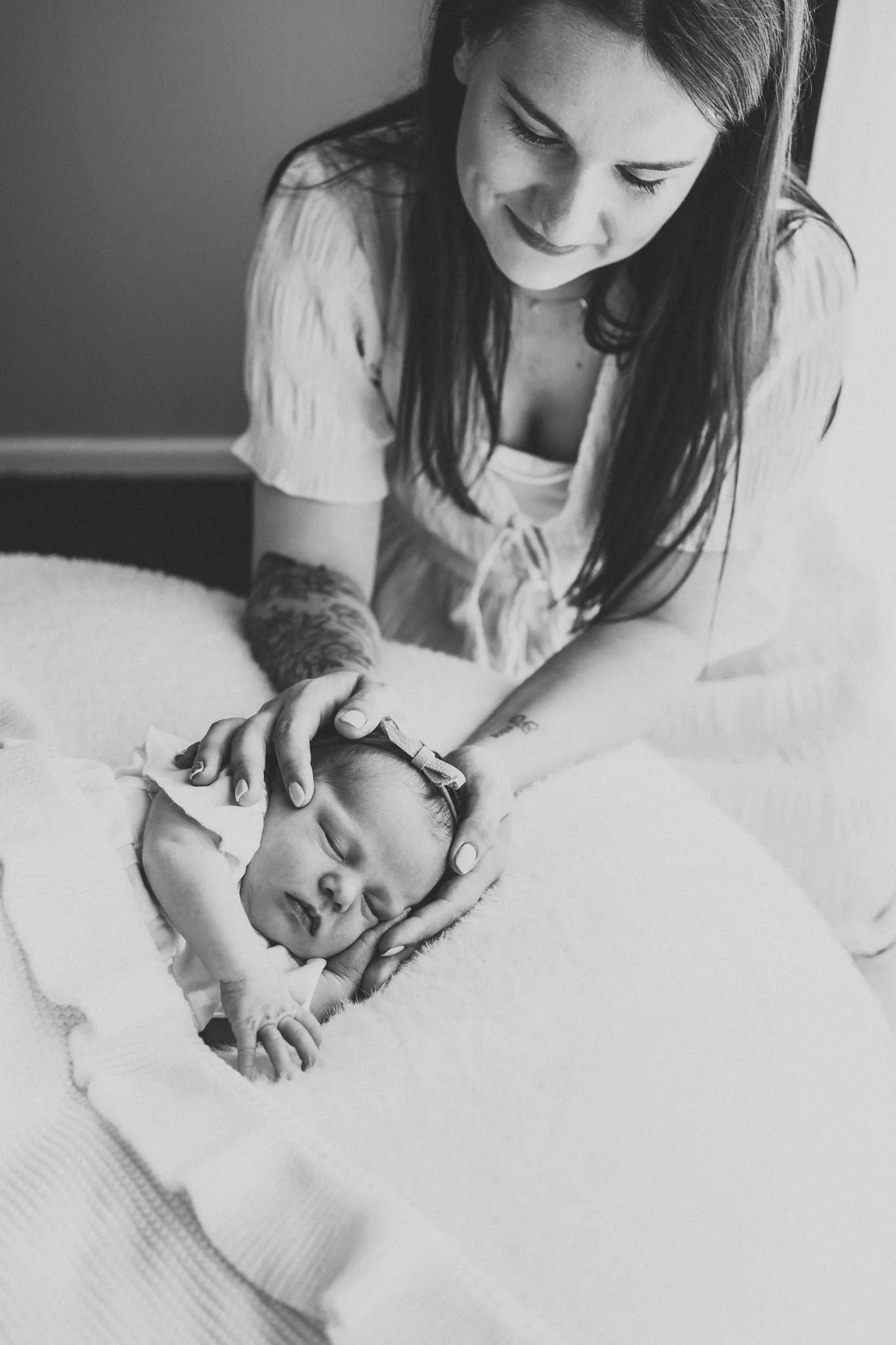 A woman looking down at a sleeping baby, gently holding the baby’s hand, in a tender and caring moment.