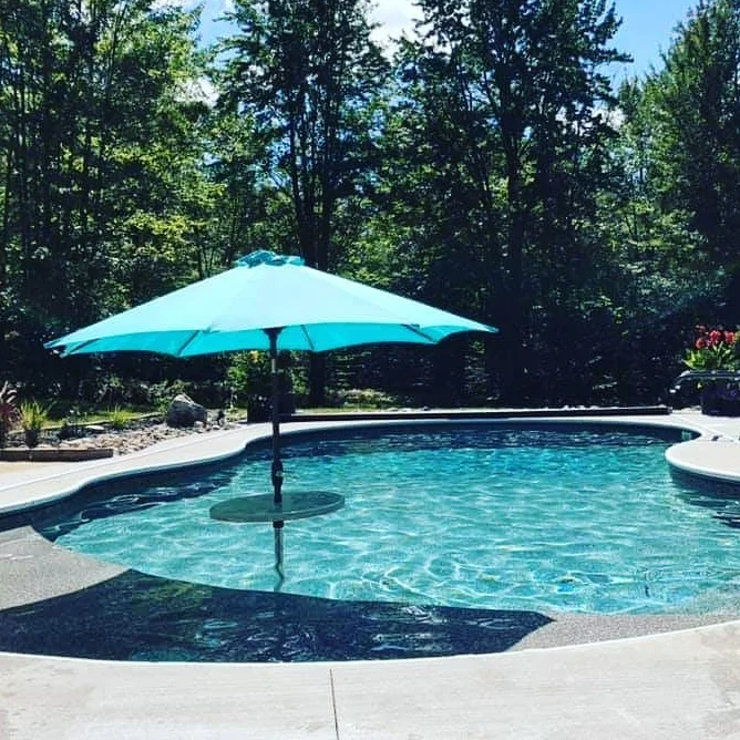Swimming pool with a large blue umbrella, surrounded by trees and landscaping.