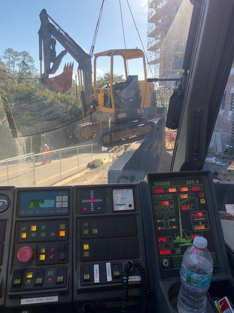 Crane lifts mini excavator machine for work positioning.