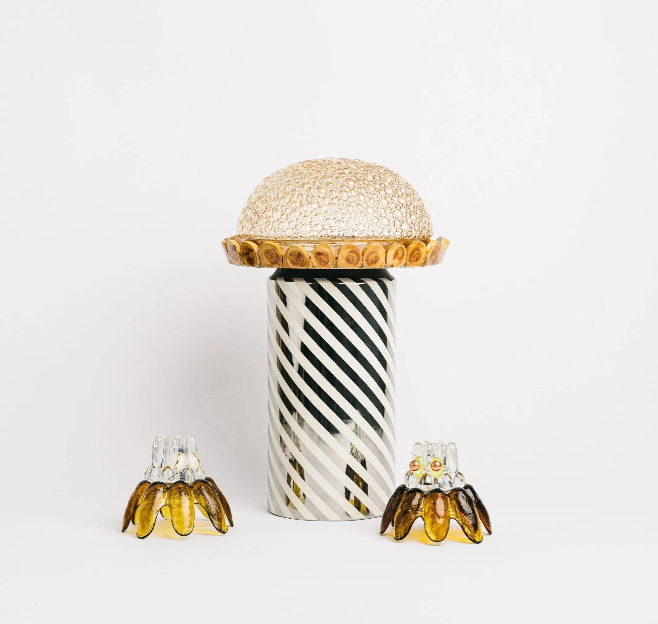 Decorative glass art sculpture featuring a tall black and white striped base, a gold-rimmed dish with a textured silver dome, and two smaller glass figures resembling flowers with yellow and amber accents.
