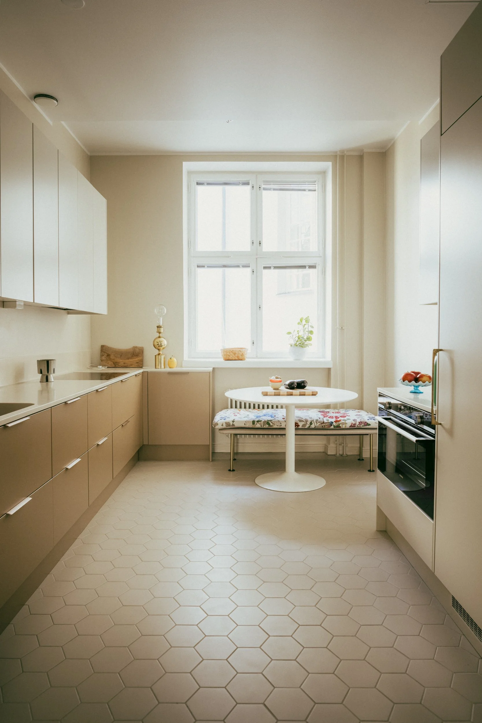 Helsinki residential interior by Studio Siru featuring a warm neutral kitchen, hexagonal tile floor, custom cabinetry and dining nook.