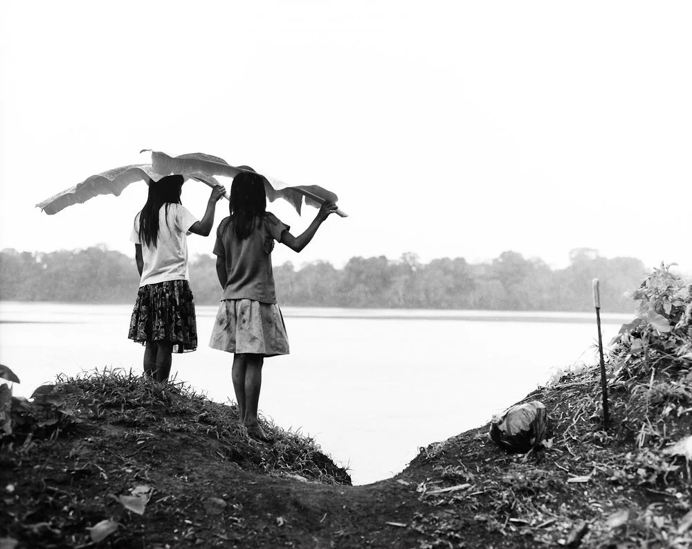 Two girls from the tribe of the Chuars standing in the rain with palm leaves over their heads, overlooking the Rio Pastaza.