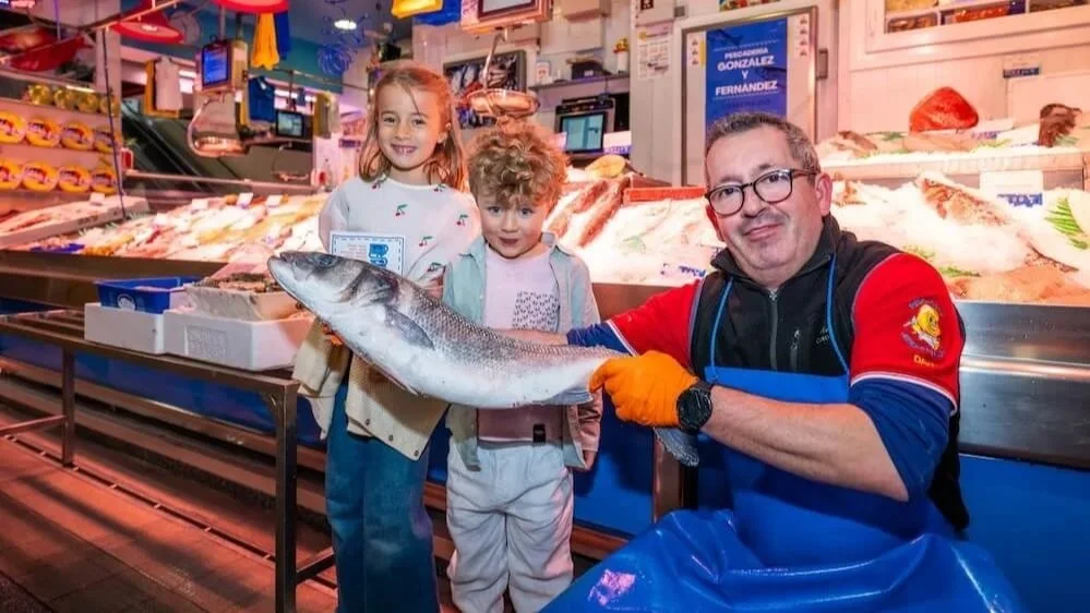 A fishmonger shows a giant fresh fish to two kids on a Market and Food Tour for Families in Madrid