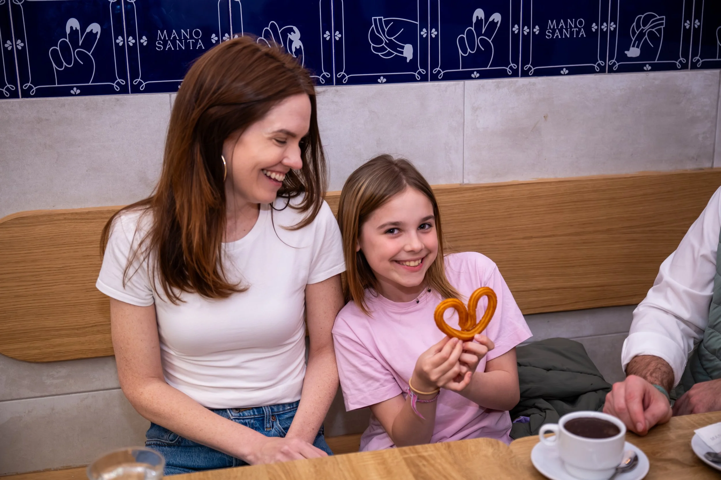 A little girl holds up a churro in the shape of a heart as her mom smiles at her on a food tour for families in Madrid.