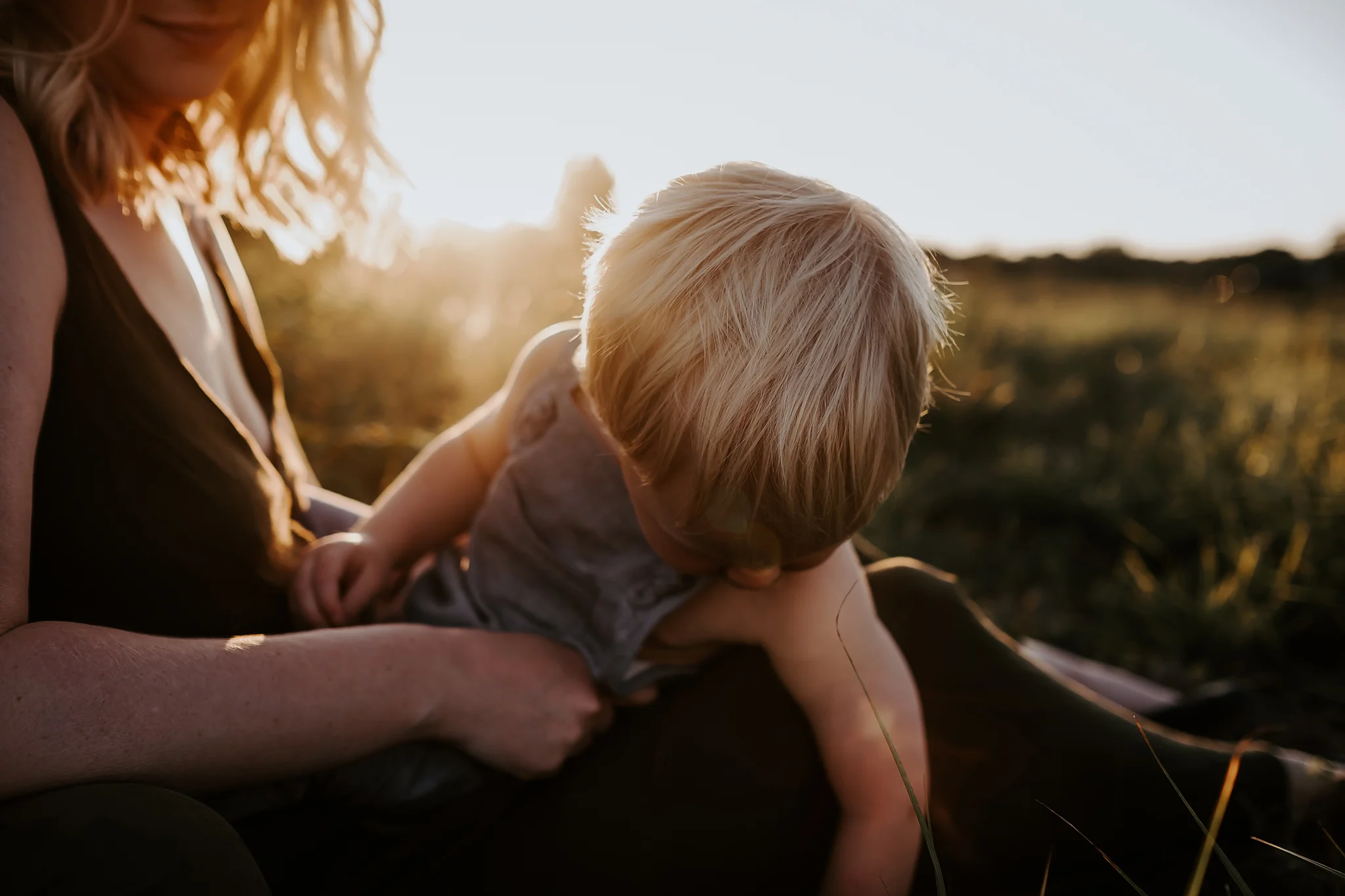 Image of a mother with her young son sitting in her lap and looking down at the grass from a family gallery by Lake Nona Florida family photographer Kristin Stefanou