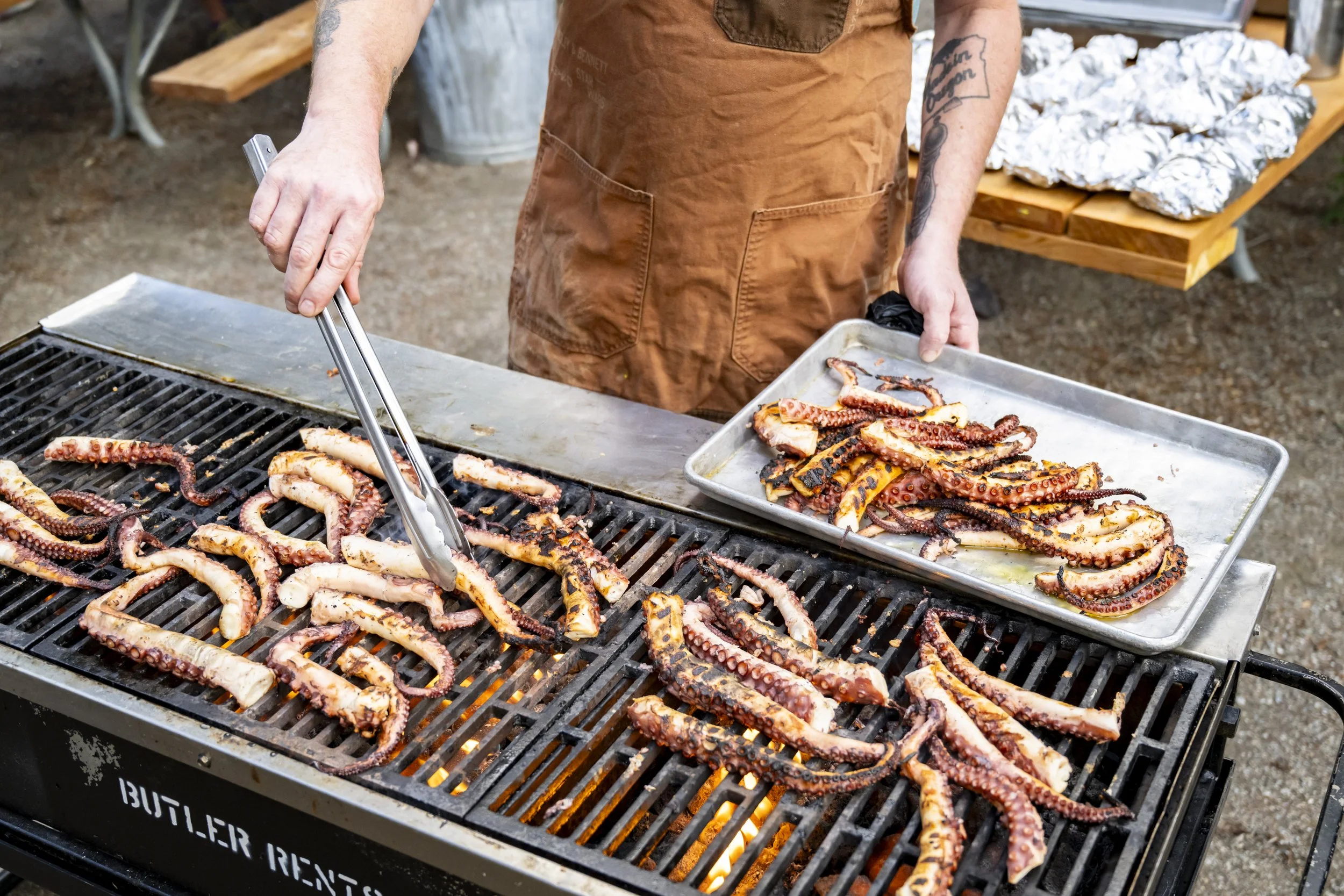 Person grilling octopus tentacles on an outdoor barbecue