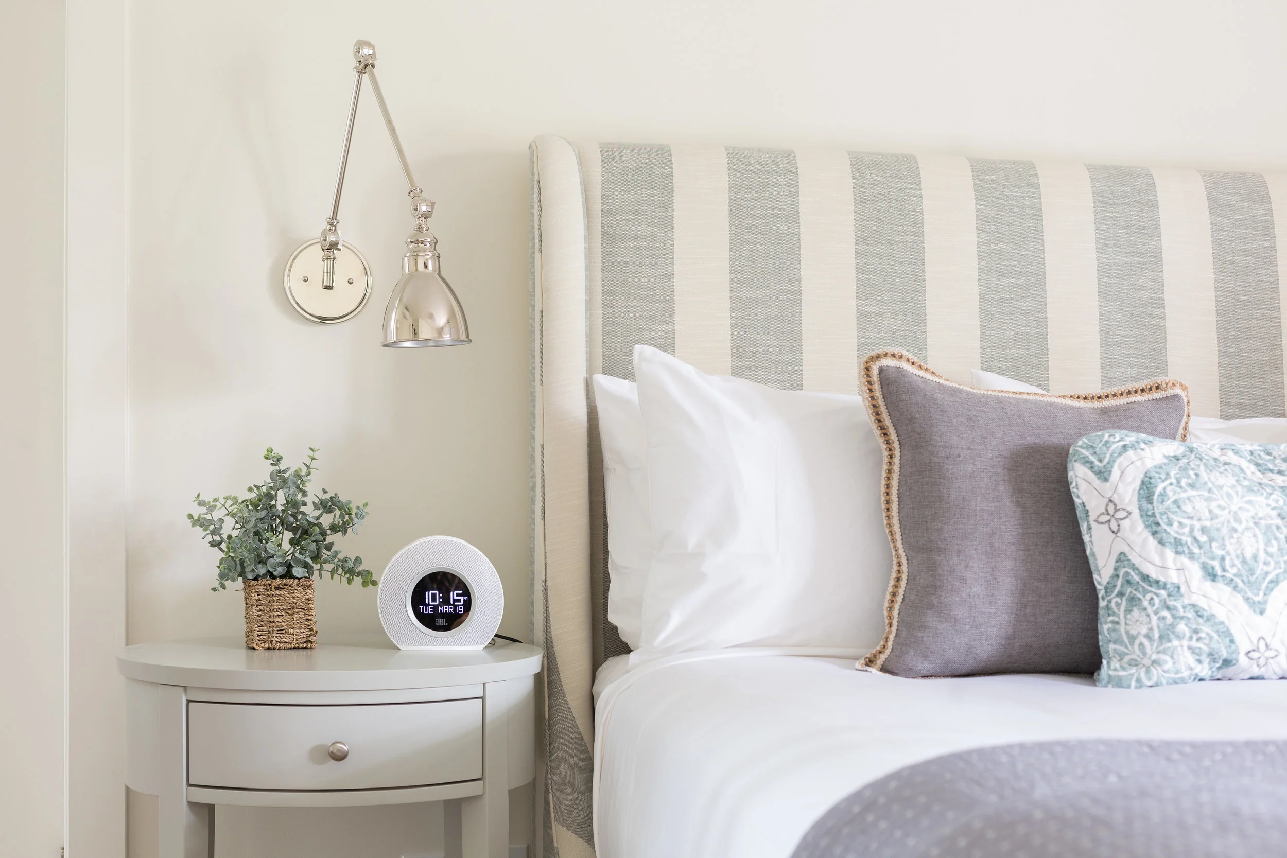 close up of bed and nightsand with plant, clock and light 