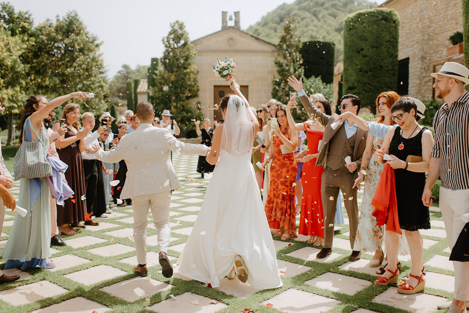 Castell de Barxell Wedding | A Romantic Spanish Countryside Celebration with Zuzanna + Raul – Zuzanna and Raul walking through a shower of pink rose petals.