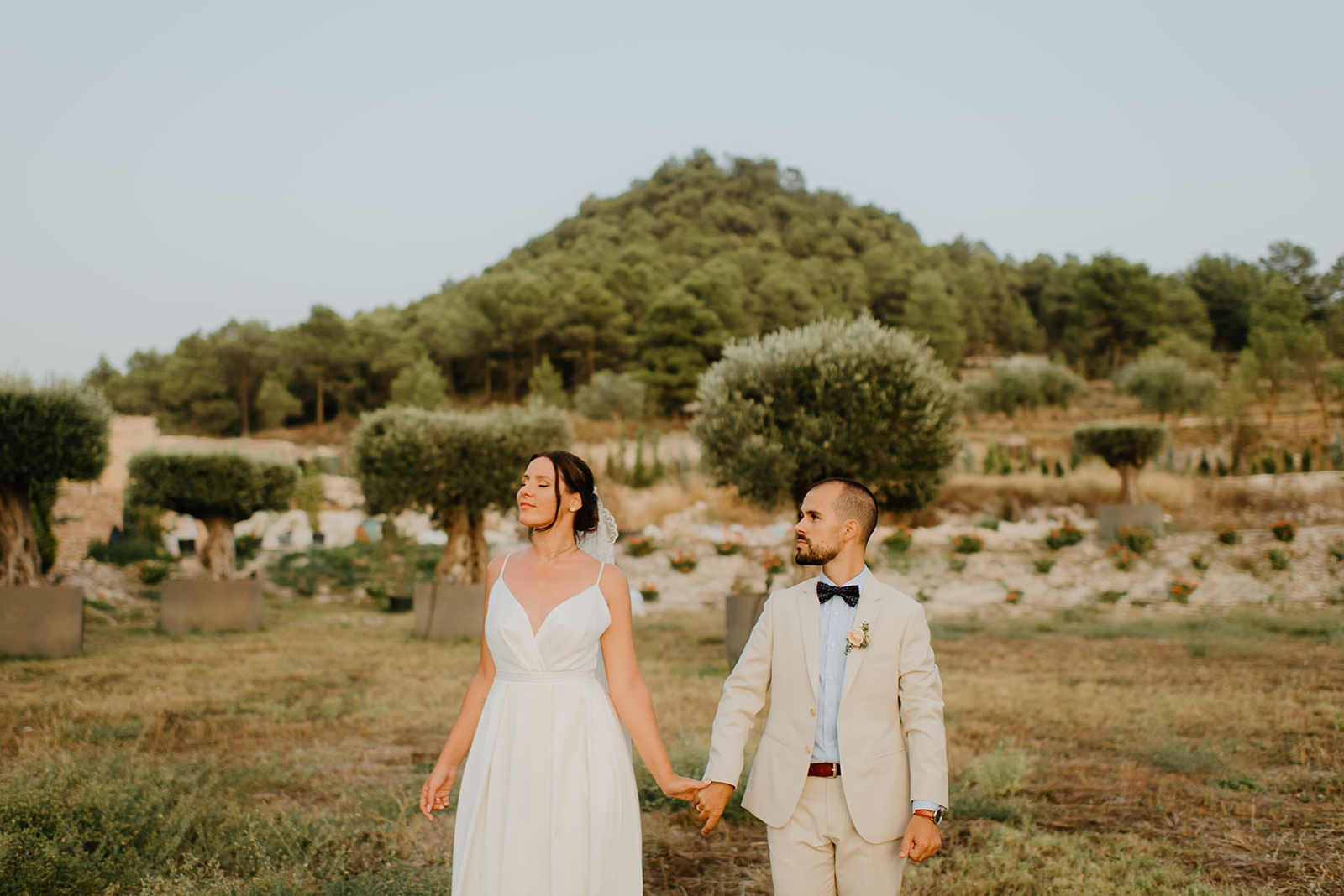 Castell de Barxell Wedding | A Romantic Spanish Countryside Celebration with Zuzanna + Raul – The couple walking hand-in-hand through an olive grove.