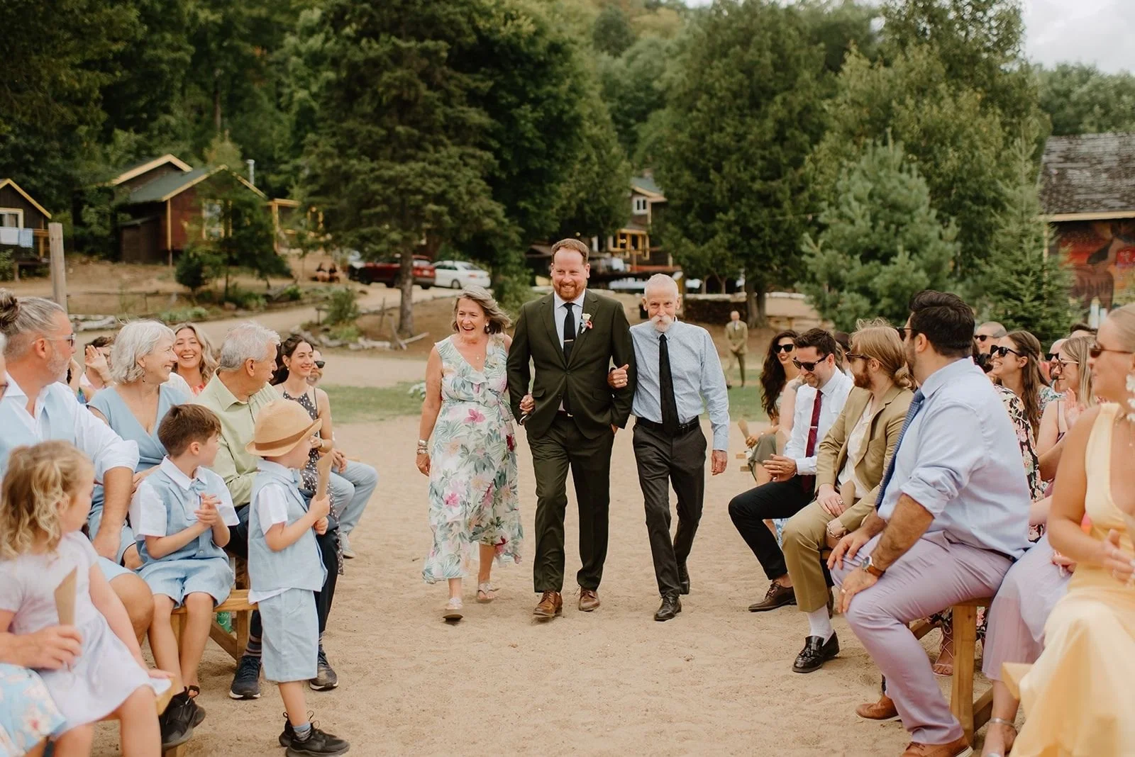 Camp Eden Woods Wedding in Ontario | Amy + Rory – Rory being escorted down the aisle by his parents during an outdoor beach ceremony in Haliburton.