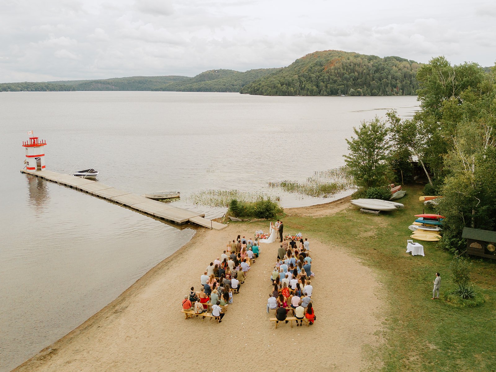 Wide view of the beach ceremony framed by sparkling lake water and lush hills