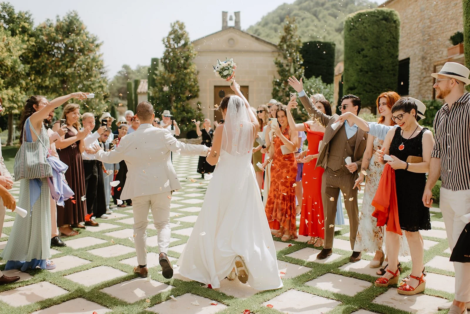 Castell de Barxell Wedding | A Romantic Spanish Countryside Celebration with Zuzanna + Raul – Zuzanna and Raul walking through a shower of pink rose petals.