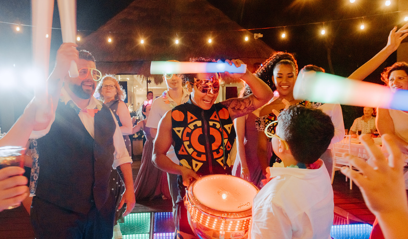 Couple enjoying a wedding reception with a lively drum performer energizing the crowd.