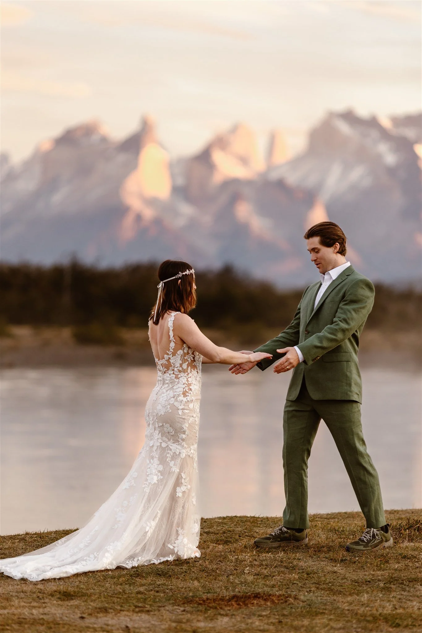The moment of their first look where the groom has turned around and sees his beautiful bride and closely examines her gorgeous lace dress with his arms out before grabbing her hands and coming in for a hug. The pink jagged mountains glow behind them