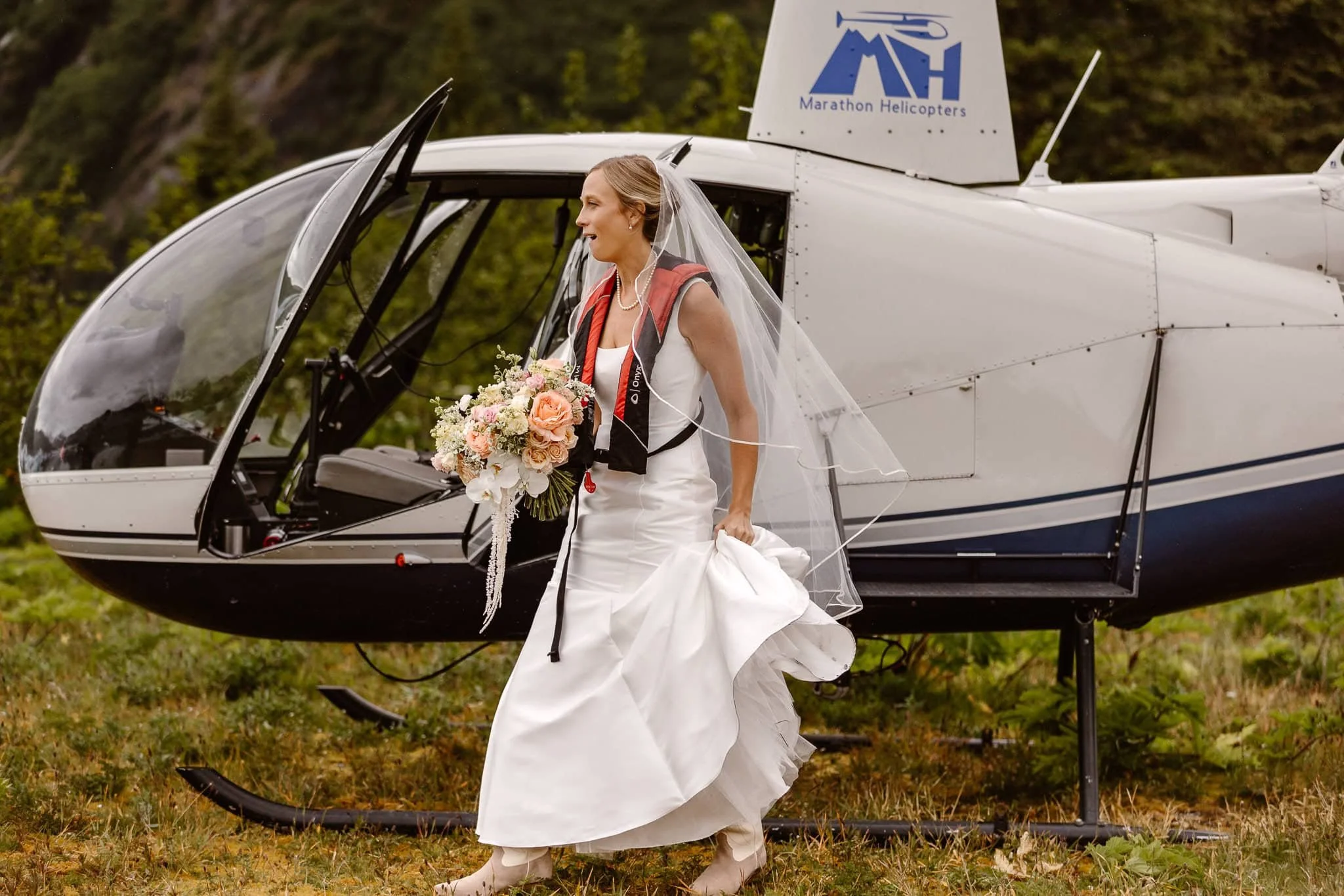 Upon her first gaze at the view they landed at, the bride is seen taking her first steps out of the helicopter, mouth agape from the spectacular site before her. She has on her tan cowboy boots and is holding her peach, white, pink, and green bouquet