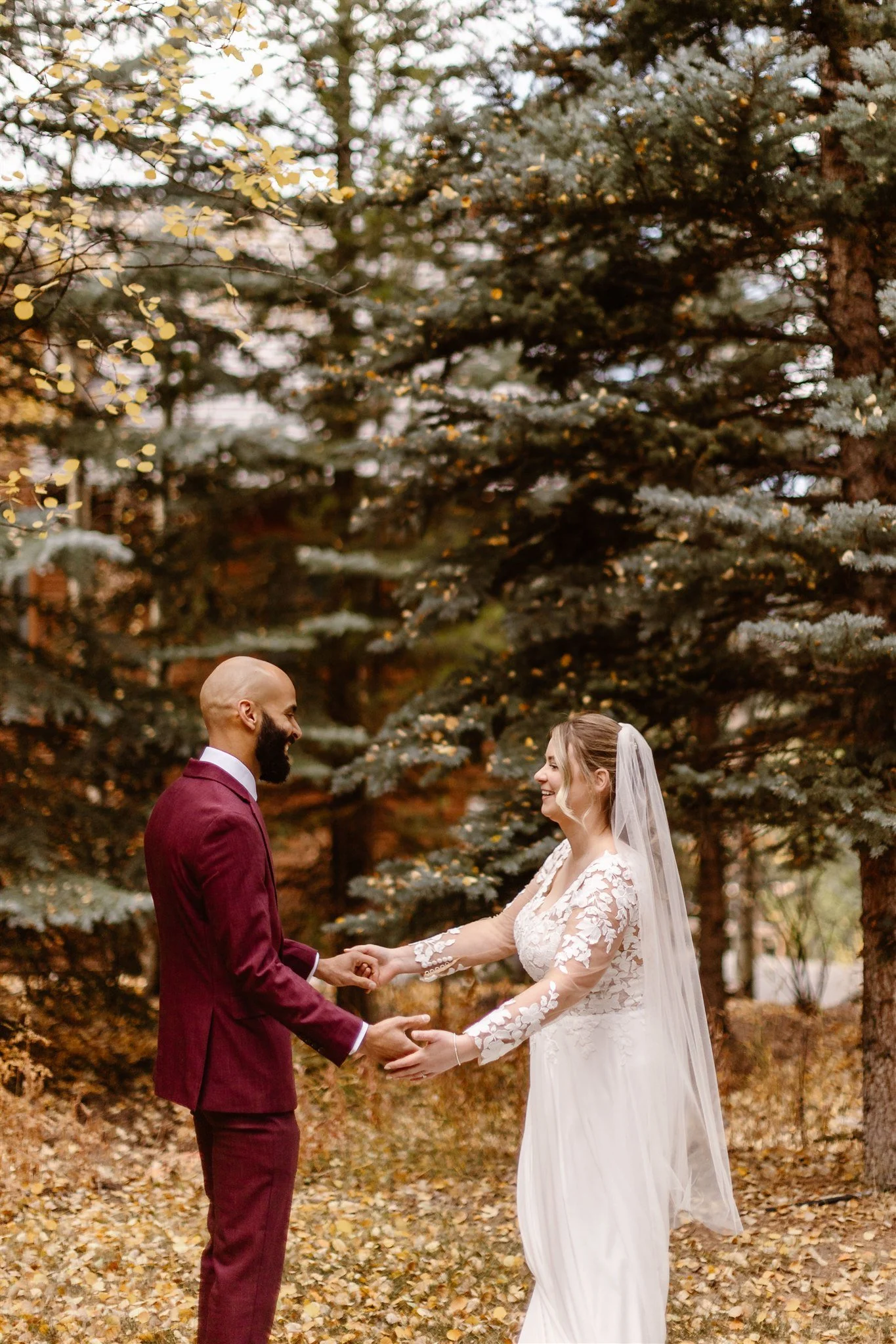 After turning around to see each other, the bride and groom both smile happily as they take in their soon-to-be spouse. The background is full of light brown fallen leaves, yellow leaves on the aspen tree to the left, and deep green of the pine trees