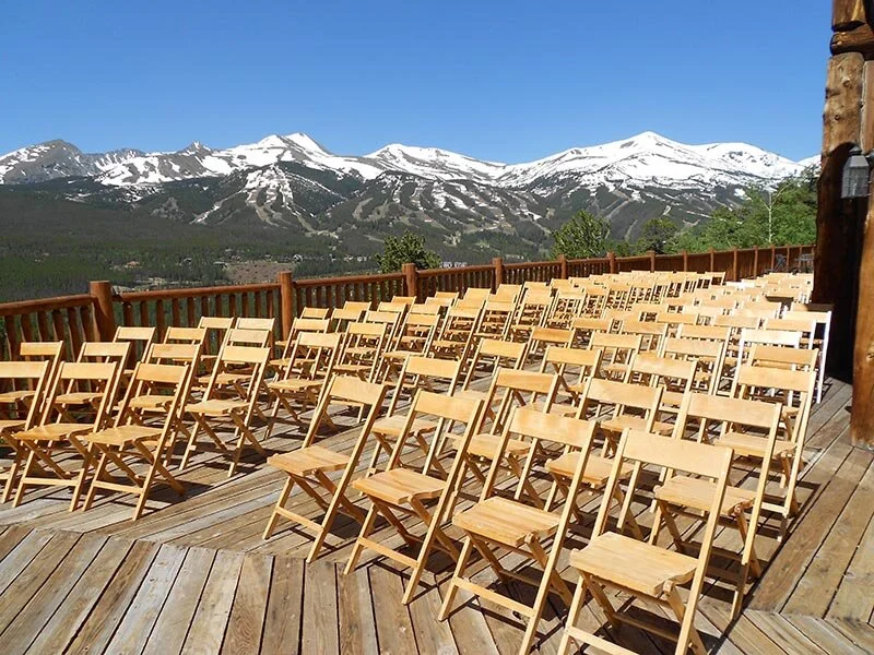 Rows of chairs are set up for a wedding ceremony with snowcapped mountain peaks in the distance