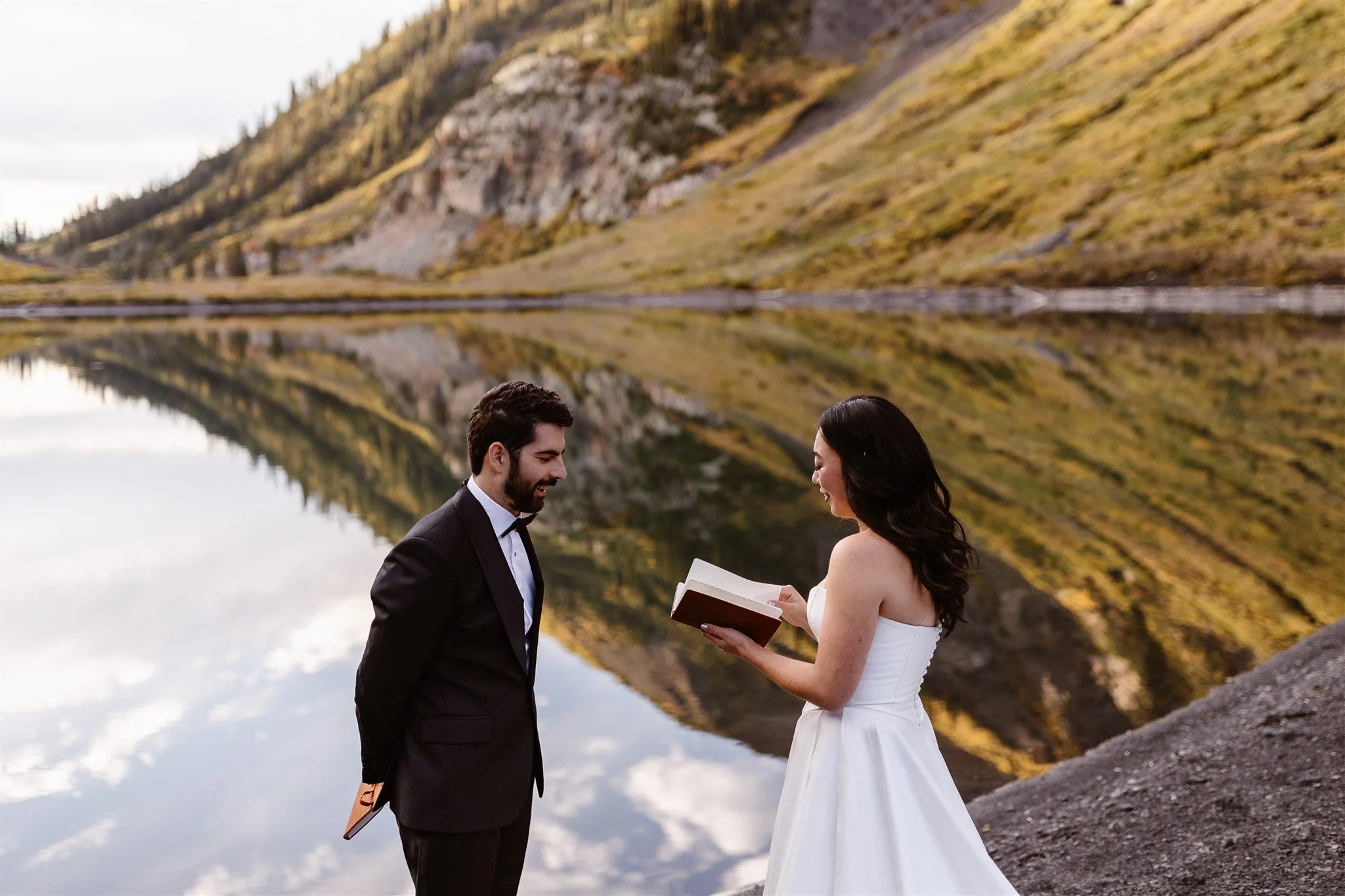 With the image of the mountains & blue sky clearly reflecting off of the lake behind them, the bride reads her vows and the grooms listens intently, with a soft smile on his face.
