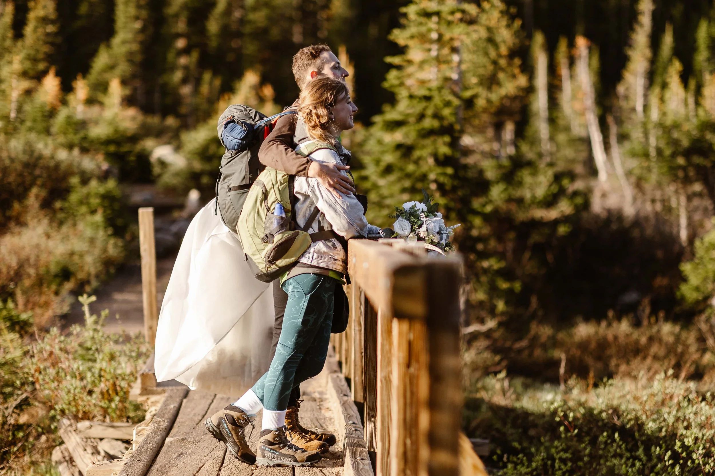 Taking a moment during their elopement hike at Lake Isabelle, the bride and groom (in their hiking clothes) take a moment to take in the gorgeous view on a nearby wooden bridge.
