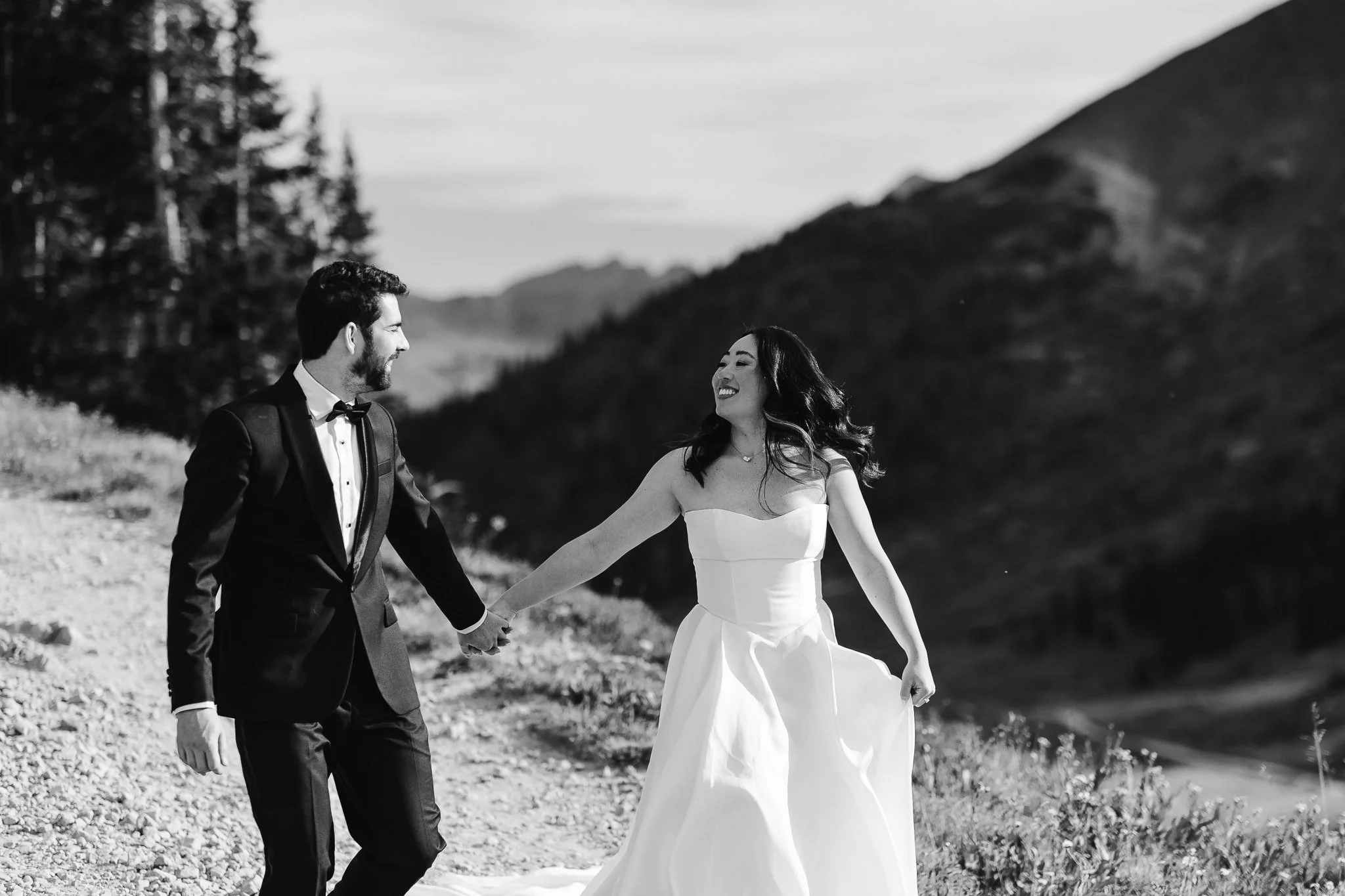 A black and white image of the two holding hands while walking down a trail to their next destination. The two are sporting wide, infectious smiles while looking at each other.