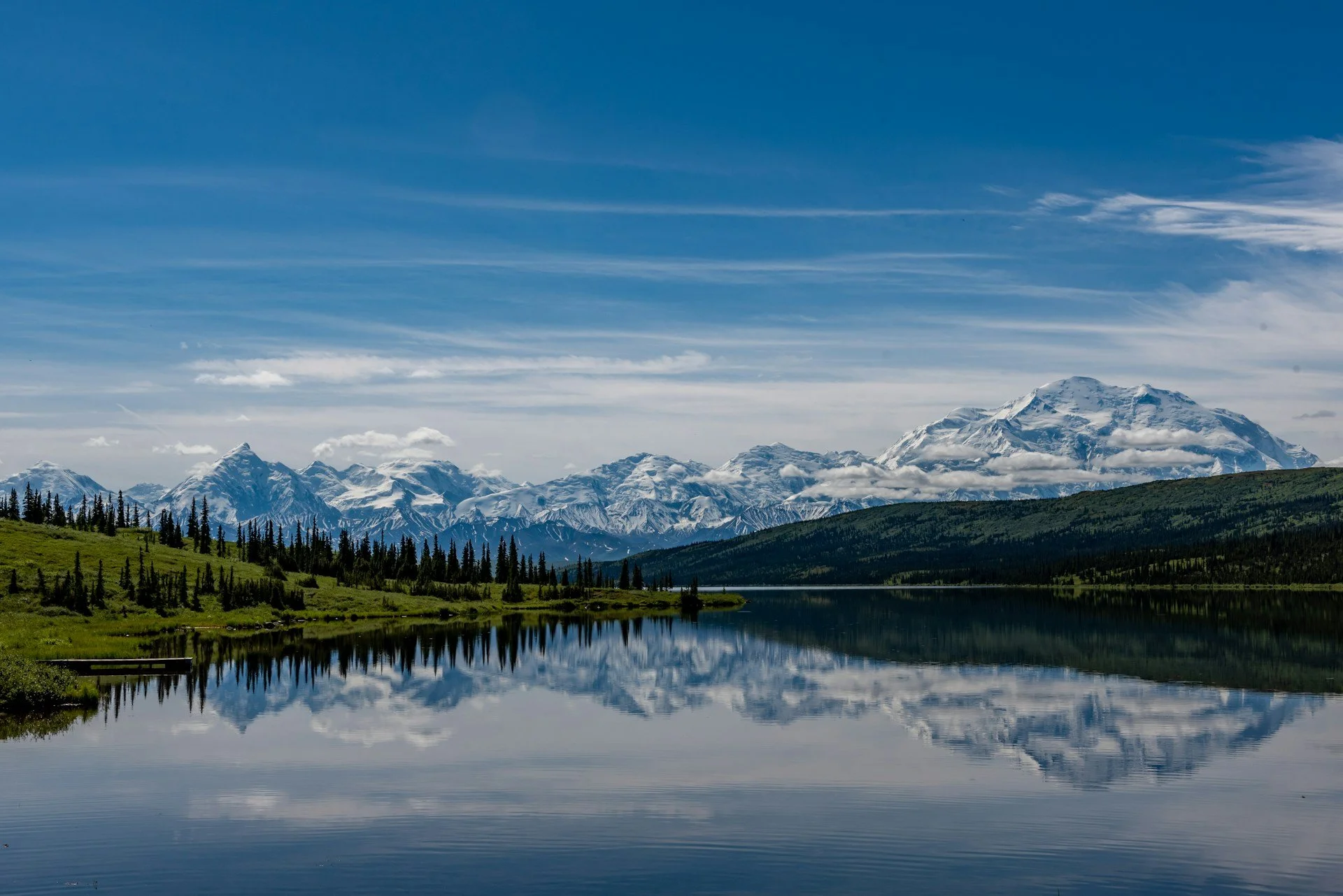 A stunning photo of the snow-covered mountains of Denali National Park. The mountains appear blue and white and reflect almost perfectly off of the lake below.