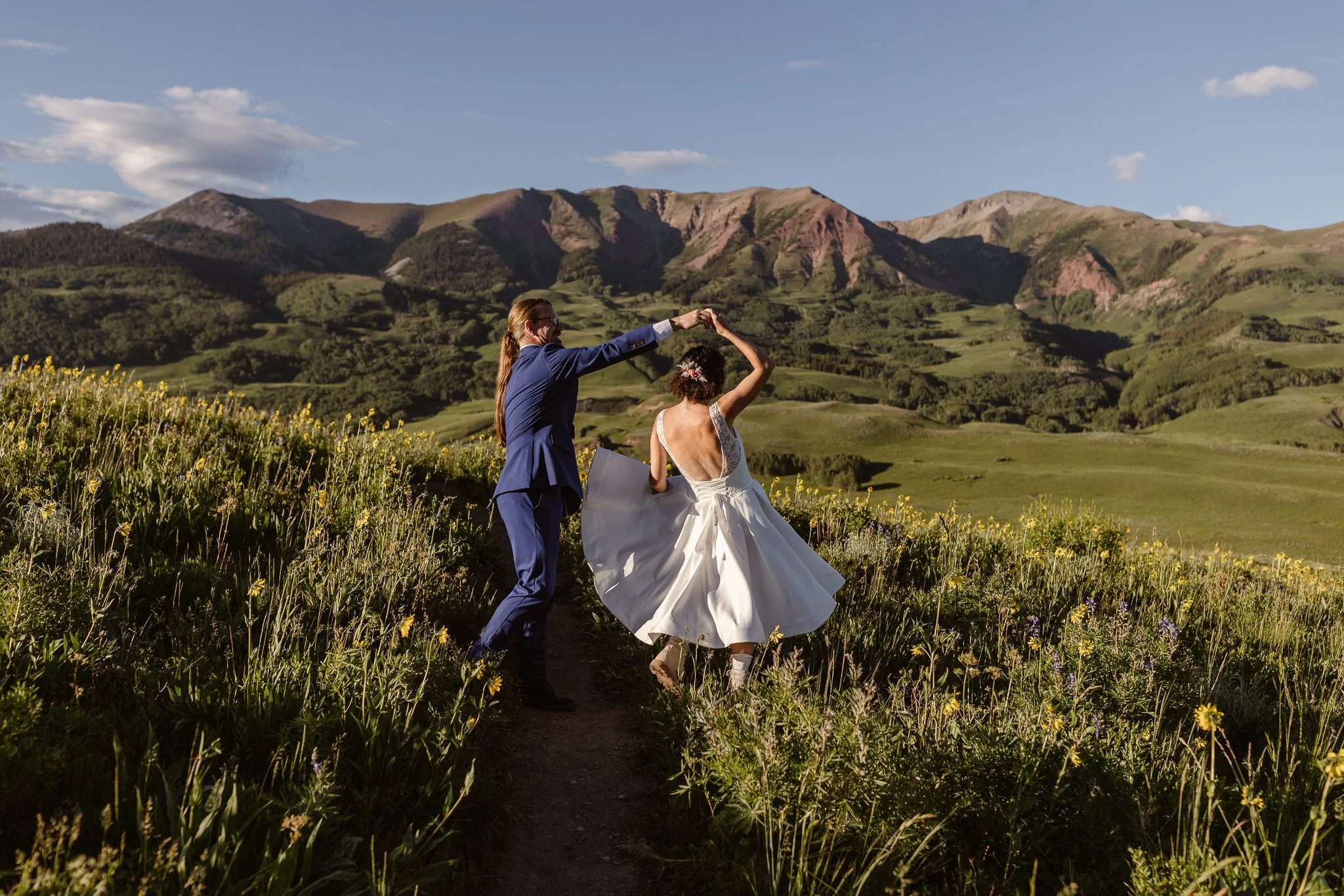 Dancing in a field of wildflowers and lush landscape of Crested Butte in the summer, the groom, in his blue suit, spins his new wife, in her teacup wedding dress, as they dance the rest of the day away.