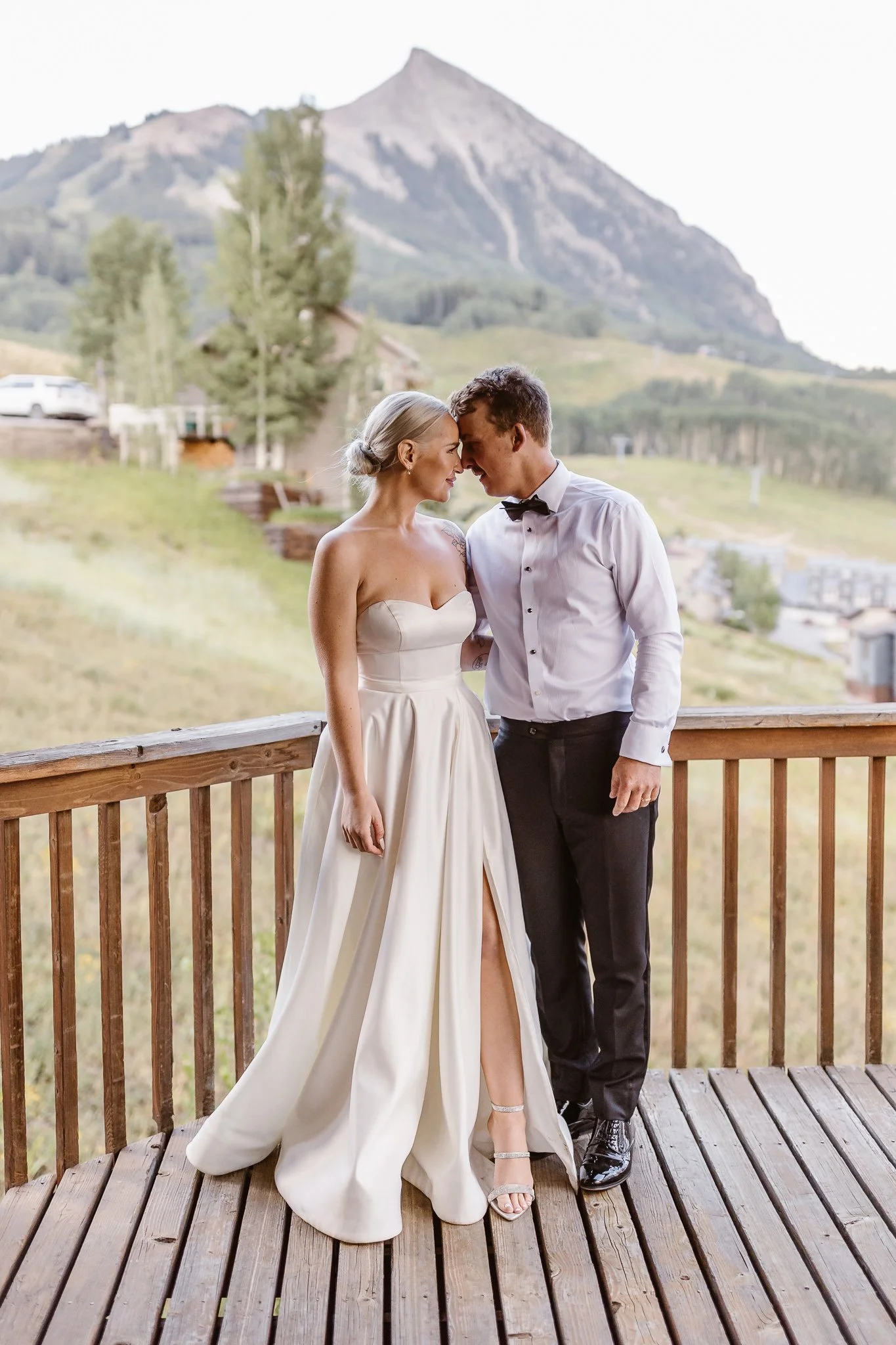 Newlyweds gaze into each other's eyes standing on a deck with a dramatic mountain peak behind them